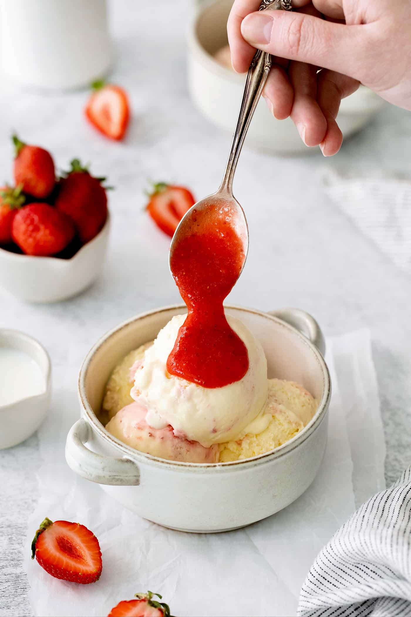 This homemade Crème Fraîche Strawberry Ice Cream is rich and ultra creamy with a gorgeous strawberry swirl folded into a tangy ice cream. A bowl of crème fraîche strawberry swirl ice cream with a spoon drizzling strawberry sauce.