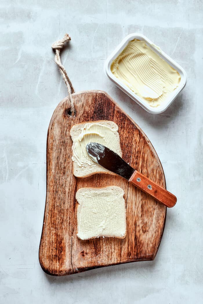 Spreading bread with butter on a cutting board.