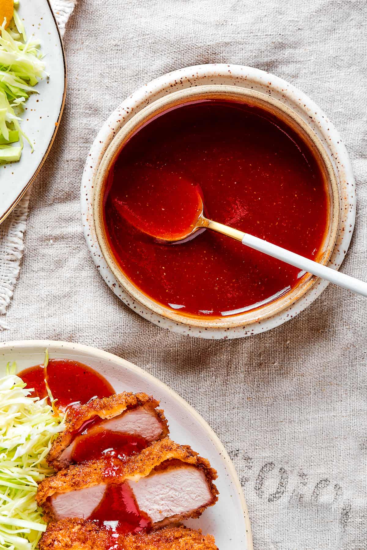 Tender, juicy Pork Katsu is always welcome on my dinner table! This Japanese dish deep fries breaded pork loin until crispy. A bowl of tonkatsu sauce with a spoon.