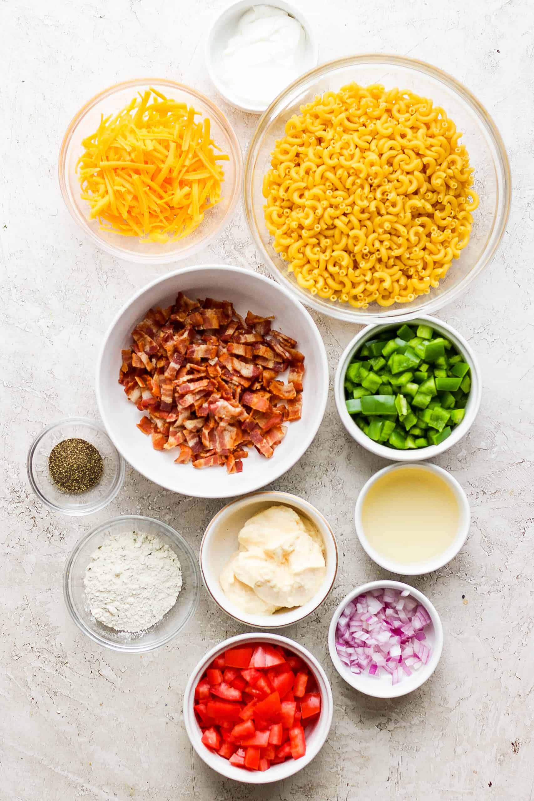 Make this crowd-pleasing Bacon Ranch Pasta Salad for your next bbq! Crispy bacon, and tender pasta will make this potluck side a new favorite. Ingredients for bacon ranch pasta salad: green onions, red onions, macaroni, cheddar cheese, pepper, and bacon.