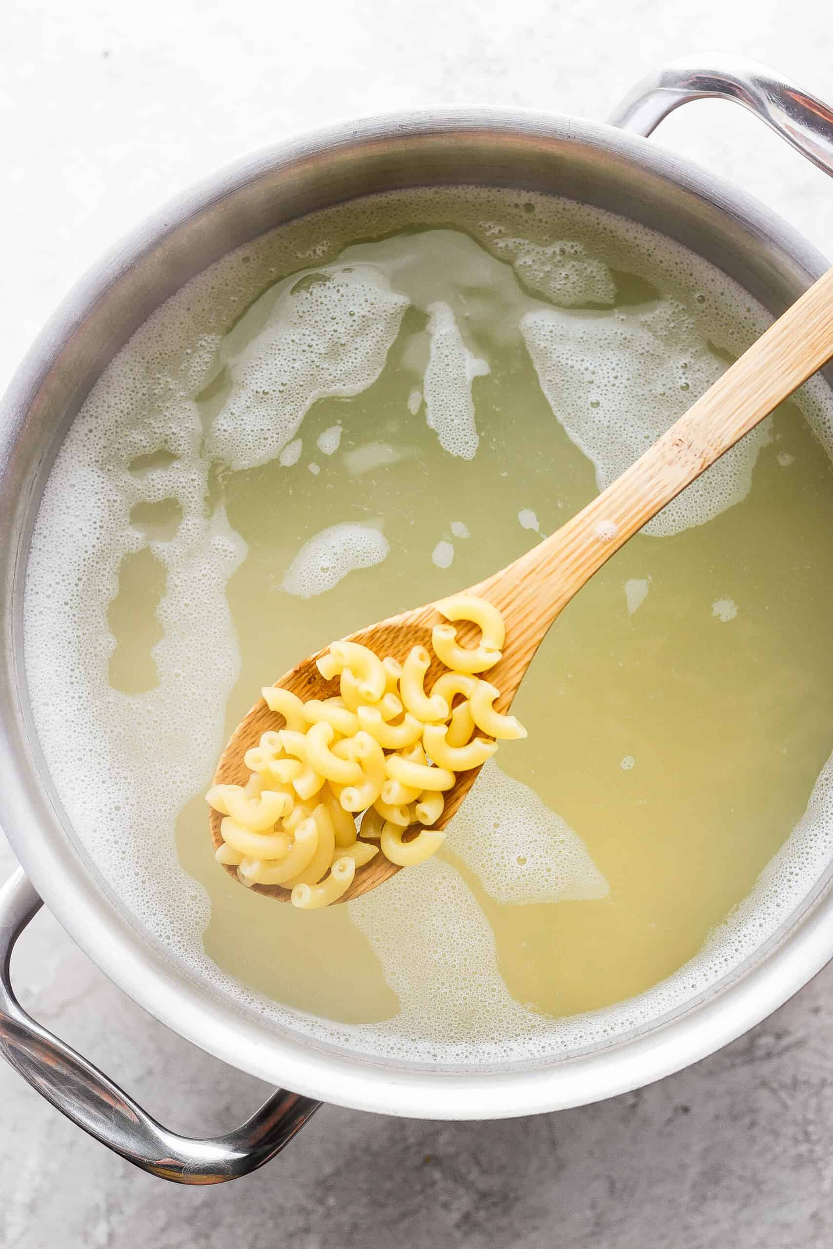 Make this crowd-pleasing Bacon Ranch Pasta Salad for your next bbq! Crispy bacon, and tender pasta will make this potluck side a new favorite. A spoon shows macaroni above a pot of water.