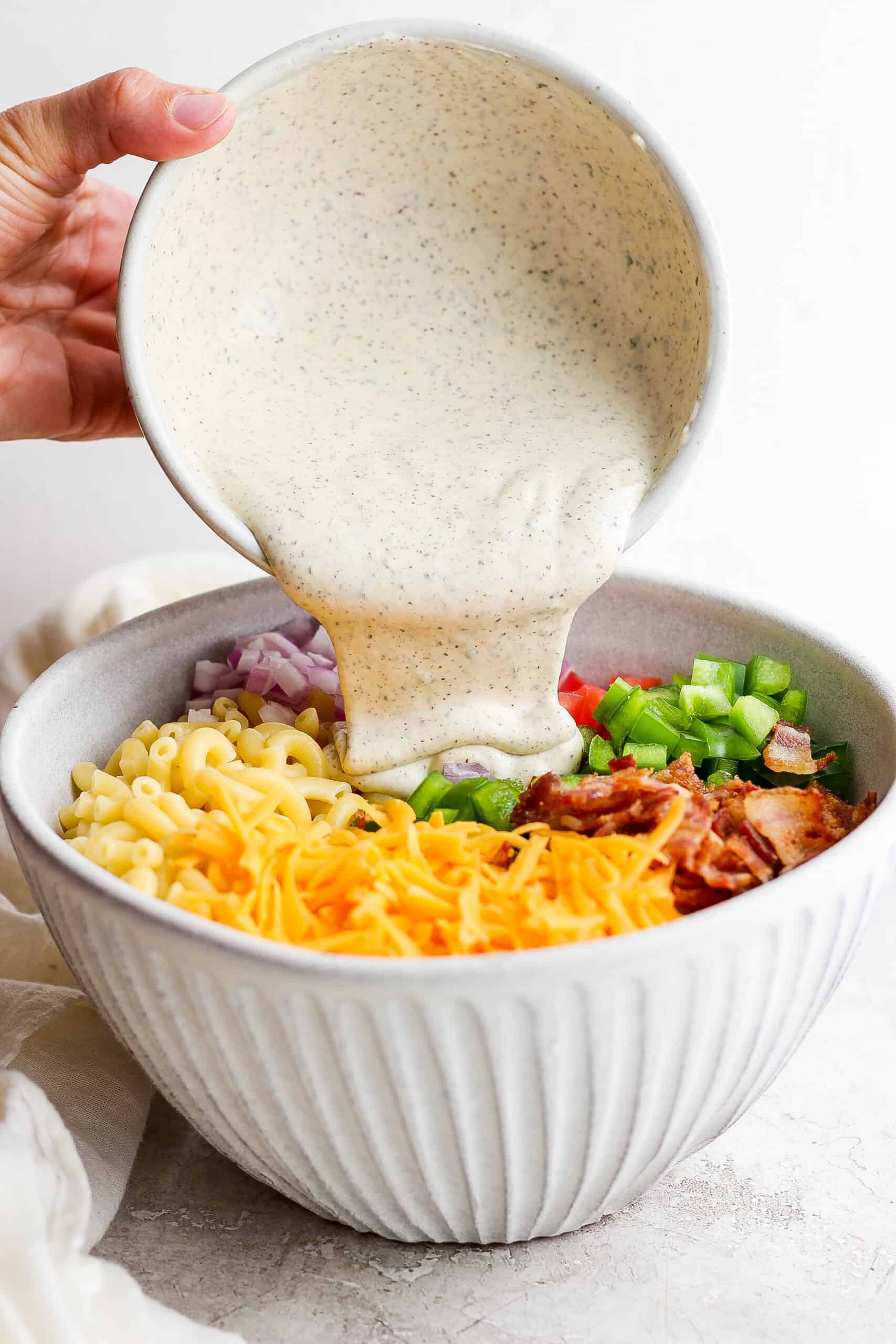 Make this crowd-pleasing Bacon Ranch Pasta Salad for your next bbq! Crispy bacon, and tender pasta will make this potluck side a new favorite. Dressing is poured into a bacon ranch pasta salad.