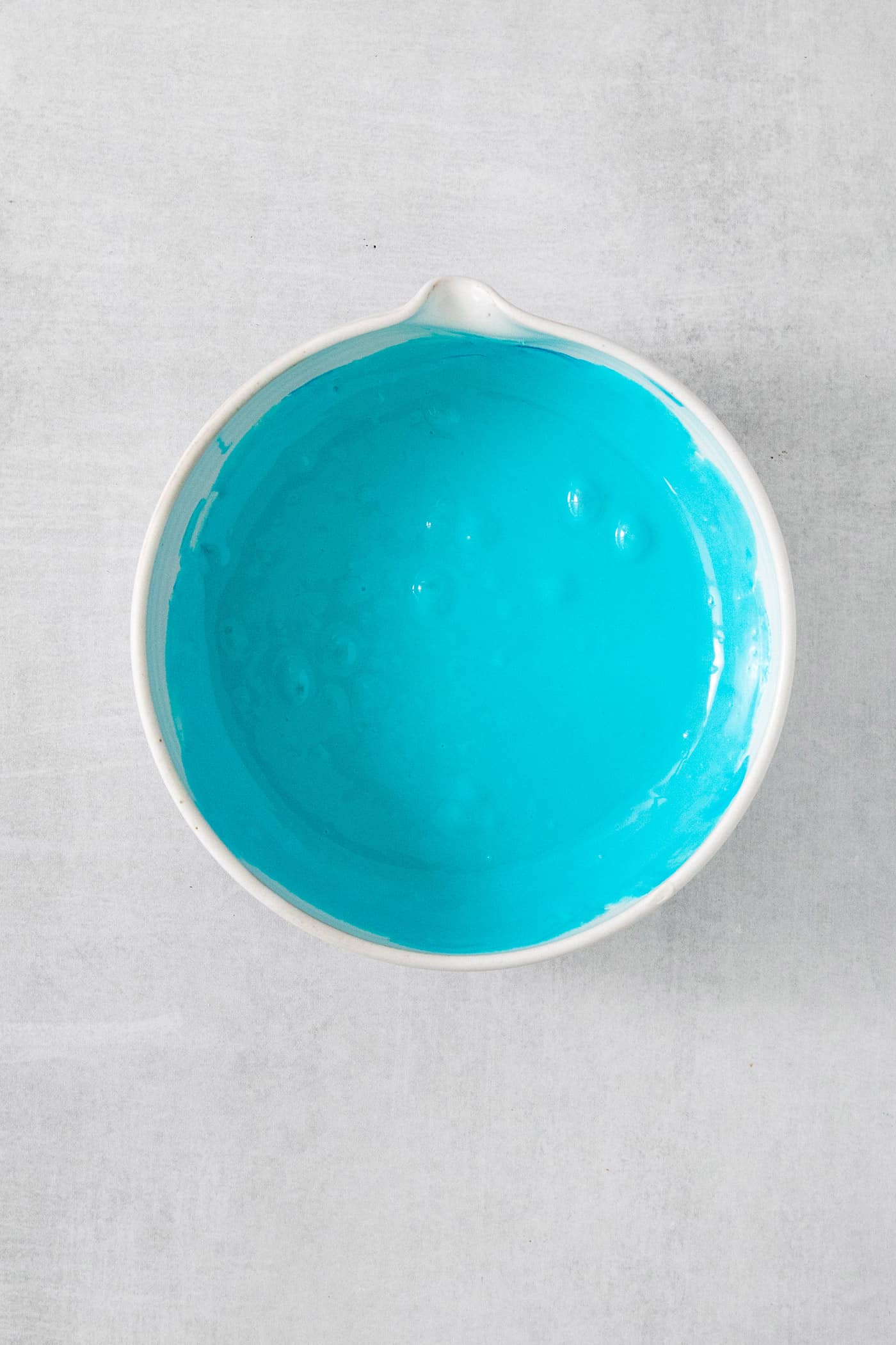 This Birthday Cake Ice Cream is delightfully rich and creamy, with swirls of blue vanilla frosting and sprinkles. No custard required! A bowl of frosting colored with blue food coloring.