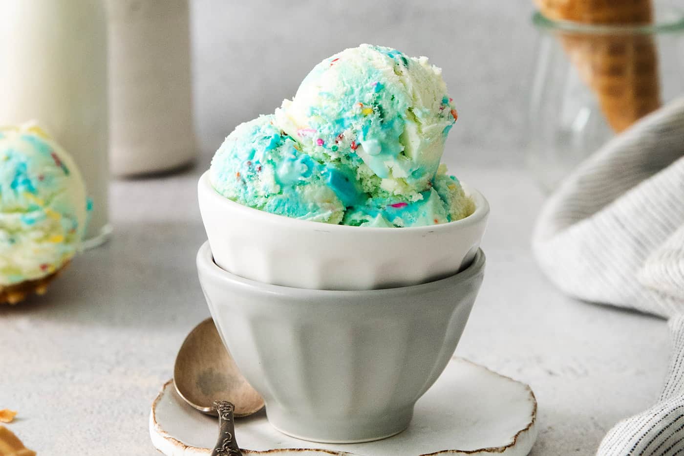 This Birthday Cake Ice Cream is delightfully rich and creamy, with swirls of blue vanilla frosting and sprinkles. No custard required! A bowl of blue birthday cake ice cream.