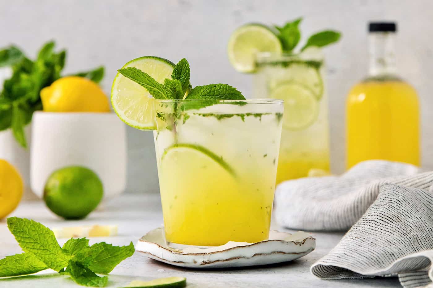 Try a Bootleg Cocktail for a citrus-infused treat of a cocktail! Lemon, lime, and orange juice combine with vodka and mint. A bootleg cocktail in a glass with mint and lime circles with fruit juice in the background.