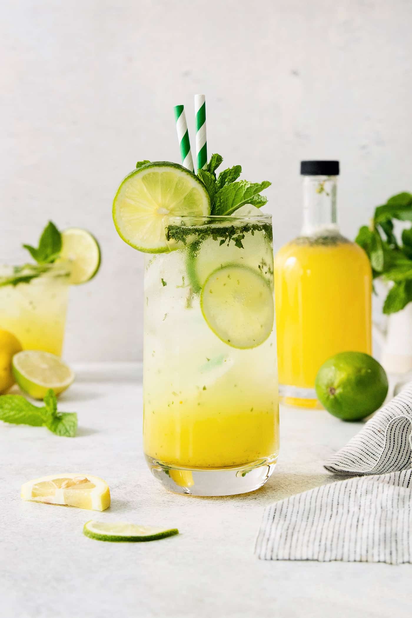 Try a Bootleg Cocktail for a citrus-infused treat of a cocktail! Lemon, lime, and orange juice combine with vodka and mint. A bootleg cocktail in a glass with straws and lime circles with fruit juice in the background.
