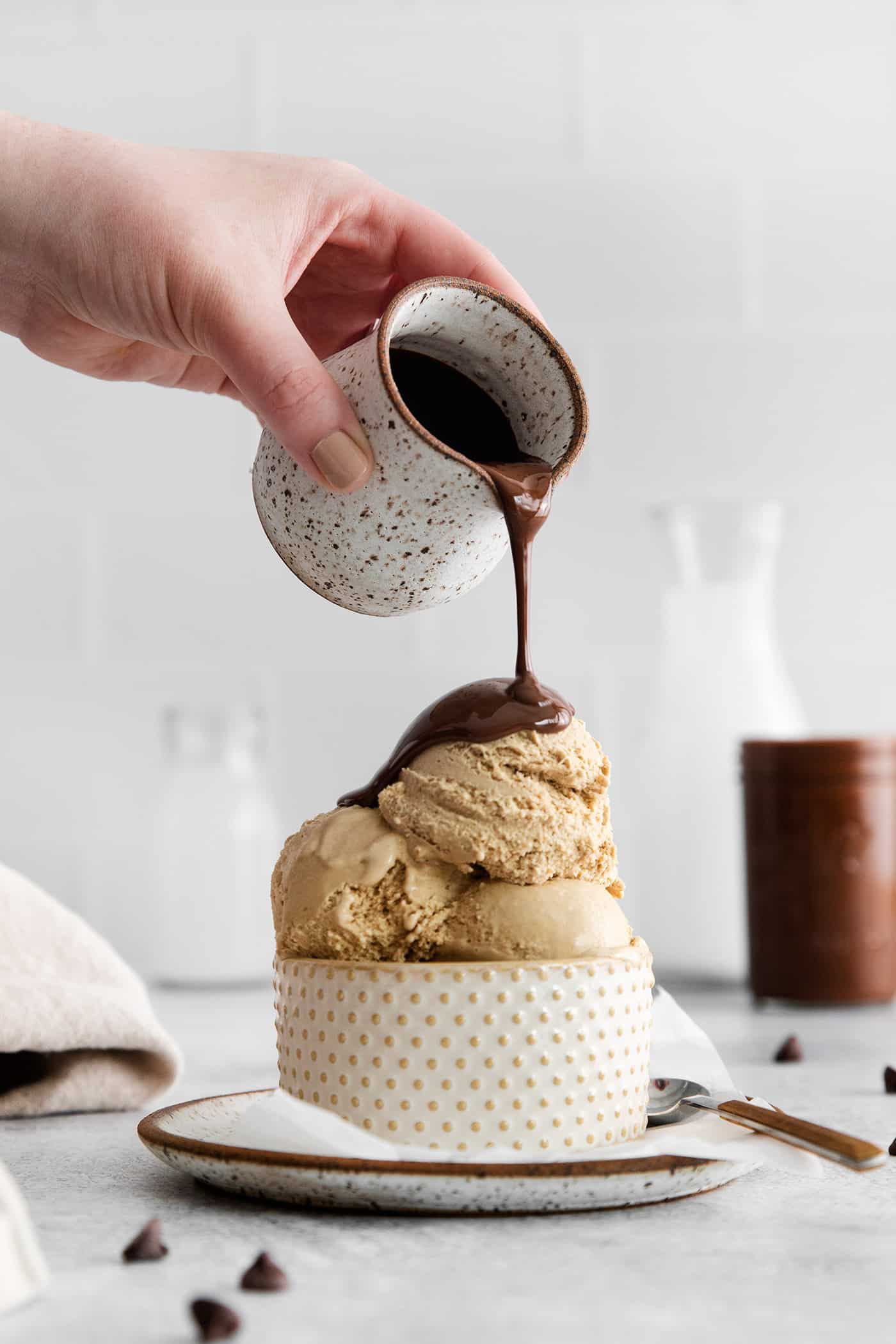 This is the easiest and best Chocolate Magic Shell recipe! Just 3 ingredients melt together to make an amazing topping. A hand pours a pitcher of magic shell over a bowl of ice cream.