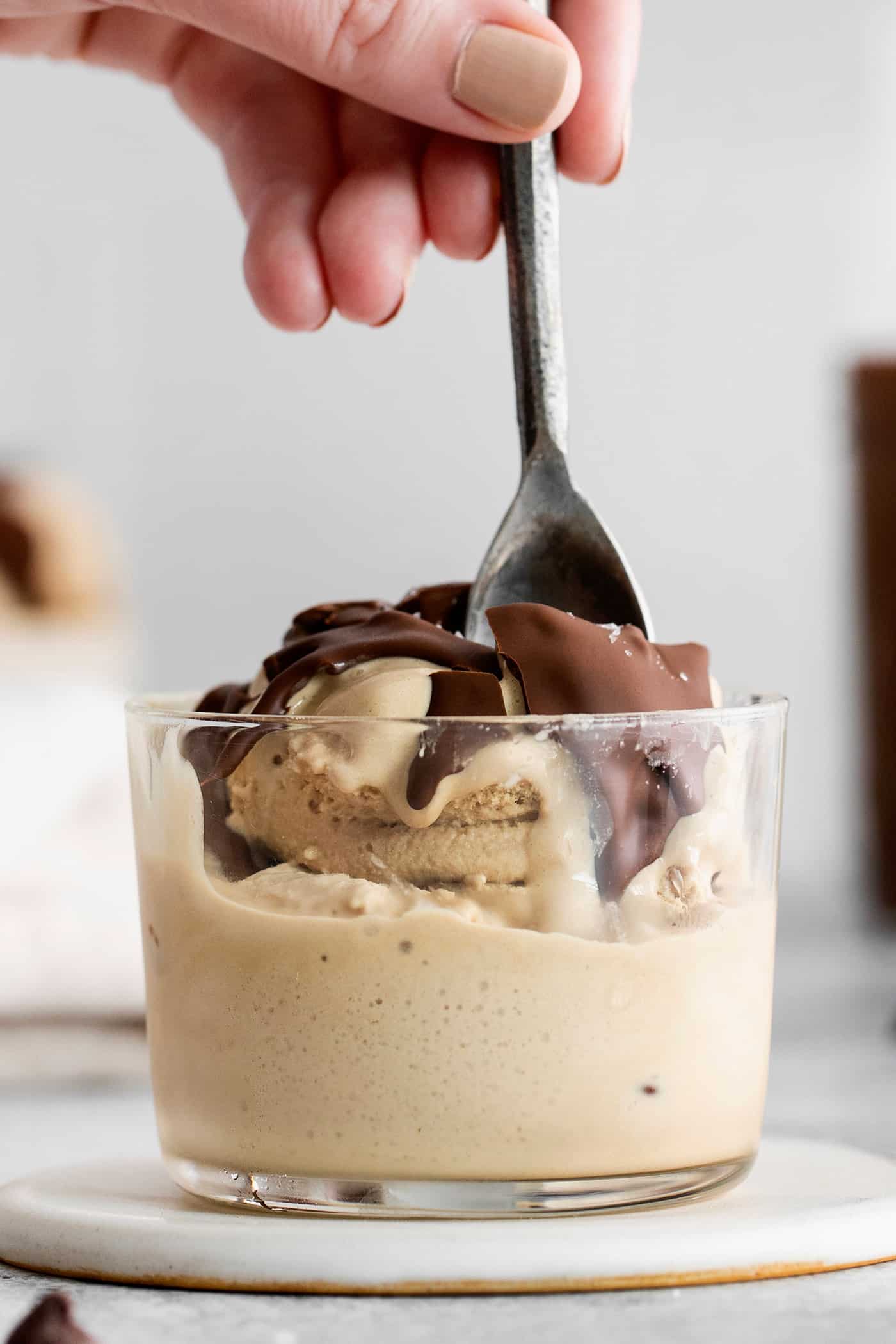This is the easiest and best Chocolate Magic Shell recipe! Just 3 ingredients melt together to make an amazing topping. A bowl of ice cream topped with magic shell and a hand holds a spoon.