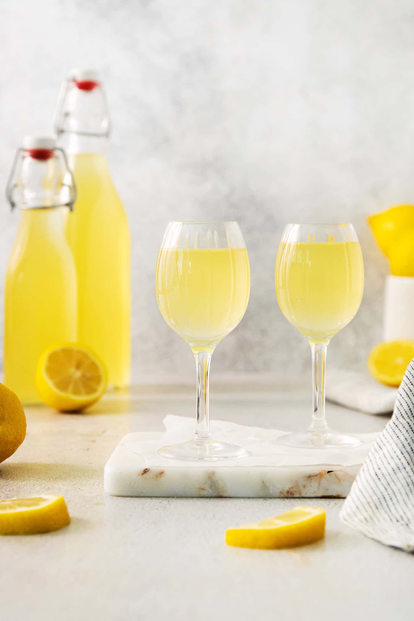 A small glass of this homemade Limoncello, served straight from the freezer, is the loveliest end to a meal. Homemade limoncello in glasses on a marble slabv with a bottle of limoncello in the background.