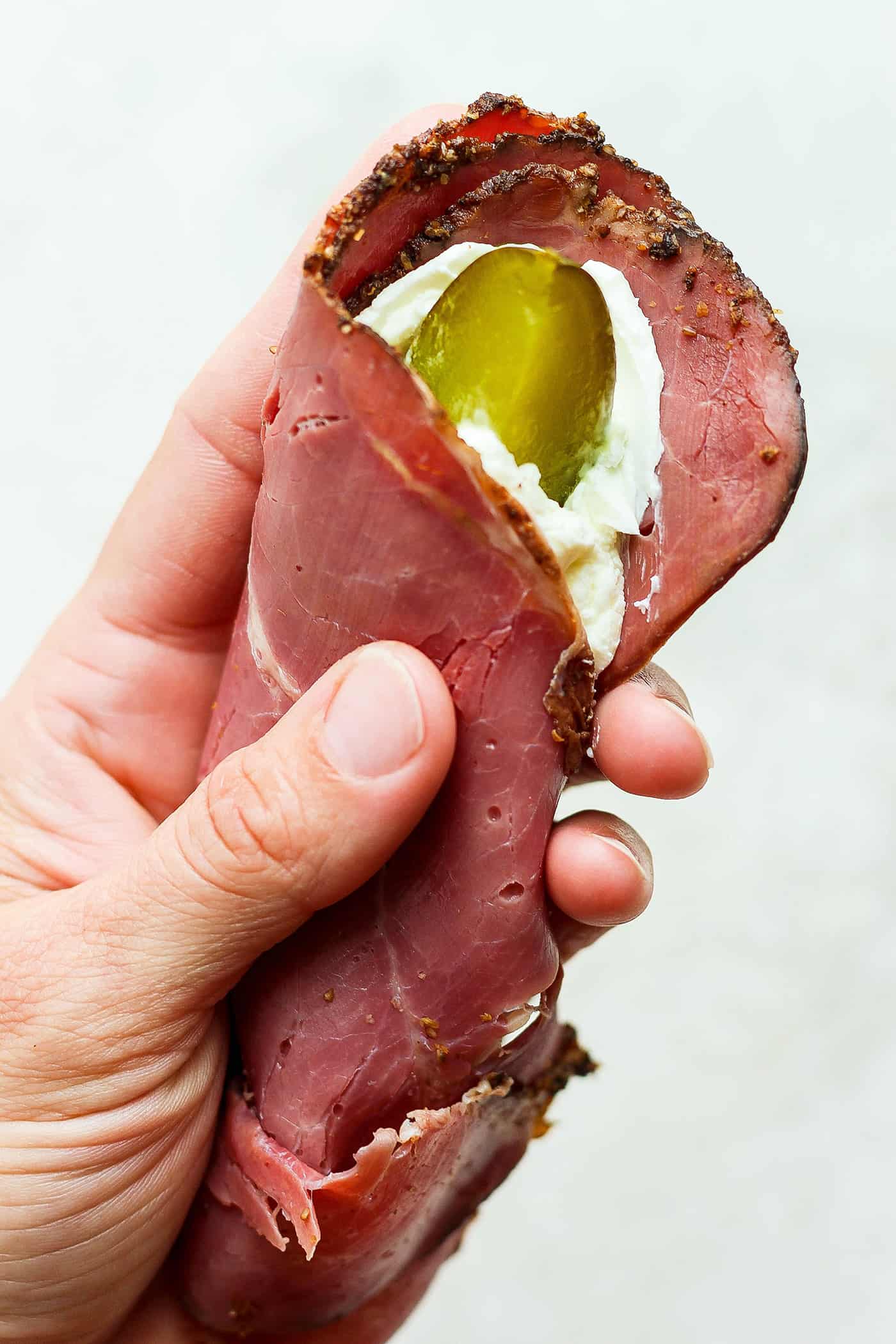 ickle Roll Ups are a 3-ingredient appetizer that's perfect for a party snack or anytime! Tangy pickles are filled with cream cheese and ham. A hand holds piece of ham spread with cream cheese with a pickle inside.