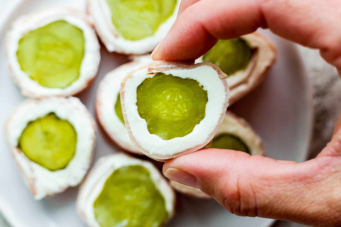 ickle Roll Ups are a 3-ingredient appetizer that's perfect for a party snack or anytime! Tangy pickles are filled with cream cheese and ham. A hand shows a pickle roll up.