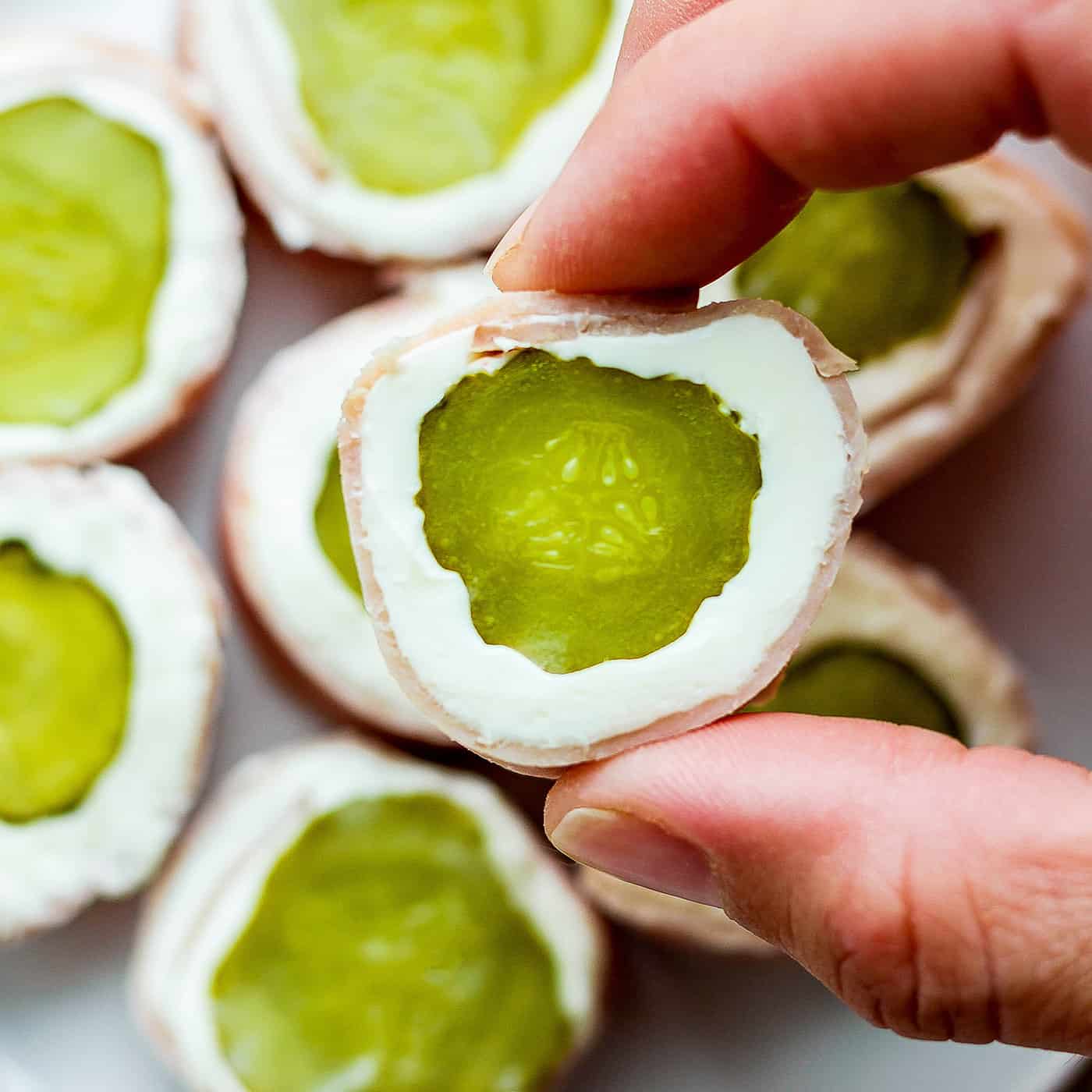 ickle Roll Ups are a 3-ingredient appetizer that's perfect for a party snack or anytime! Tangy pickles are filled with cream cheese and ham. A hand shows a pickle roll up.