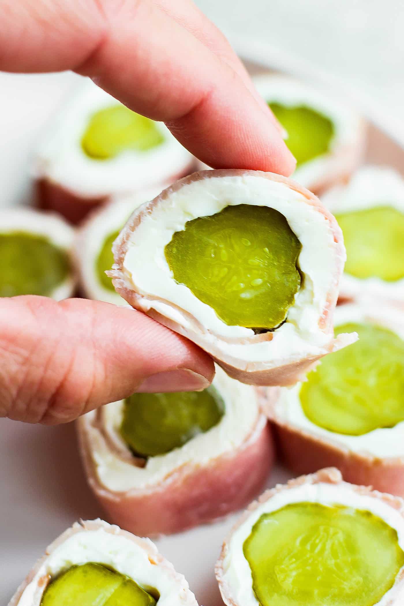 ickle Roll Ups are a 3-ingredient appetizer that's perfect for a party snack or anytime! Tangy pickles are filled with cream cheese and ham. A hand shows a pickle roll up.
