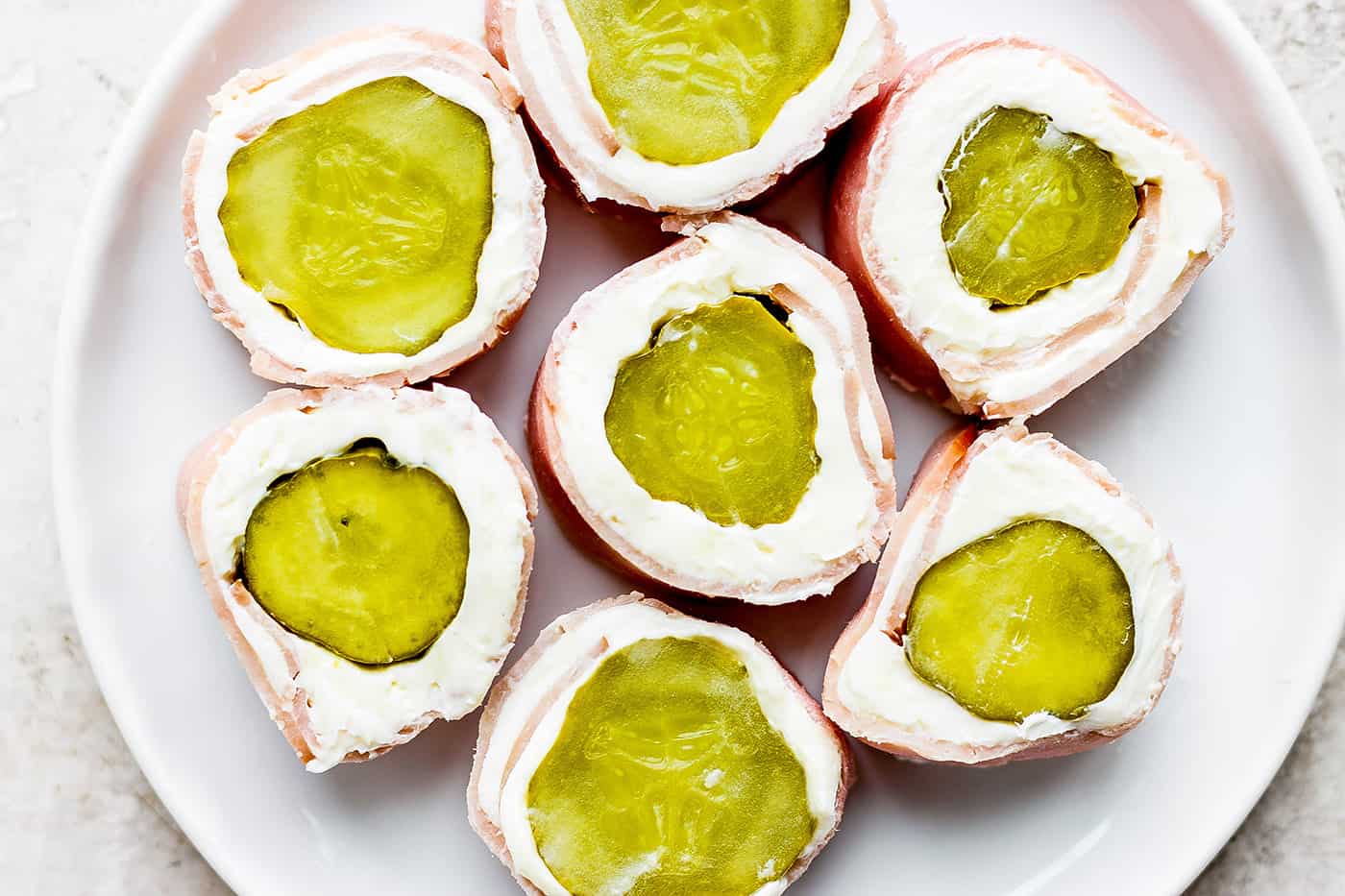 ickle Roll Ups are a 3-ingredient appetizer that's perfect for a party snack or anytime! Tangy pickles are filled with cream cheese and ham. Pickle roll up are shown on a plate.