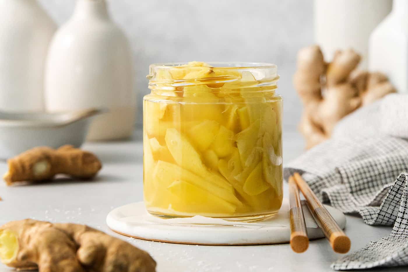 Peppery, pink Pickled Ginger is a wonderful companion to sushi and it's so easy to make at home! You need just 5 ingredients. A jar of pickled ginger with ginger in the background.