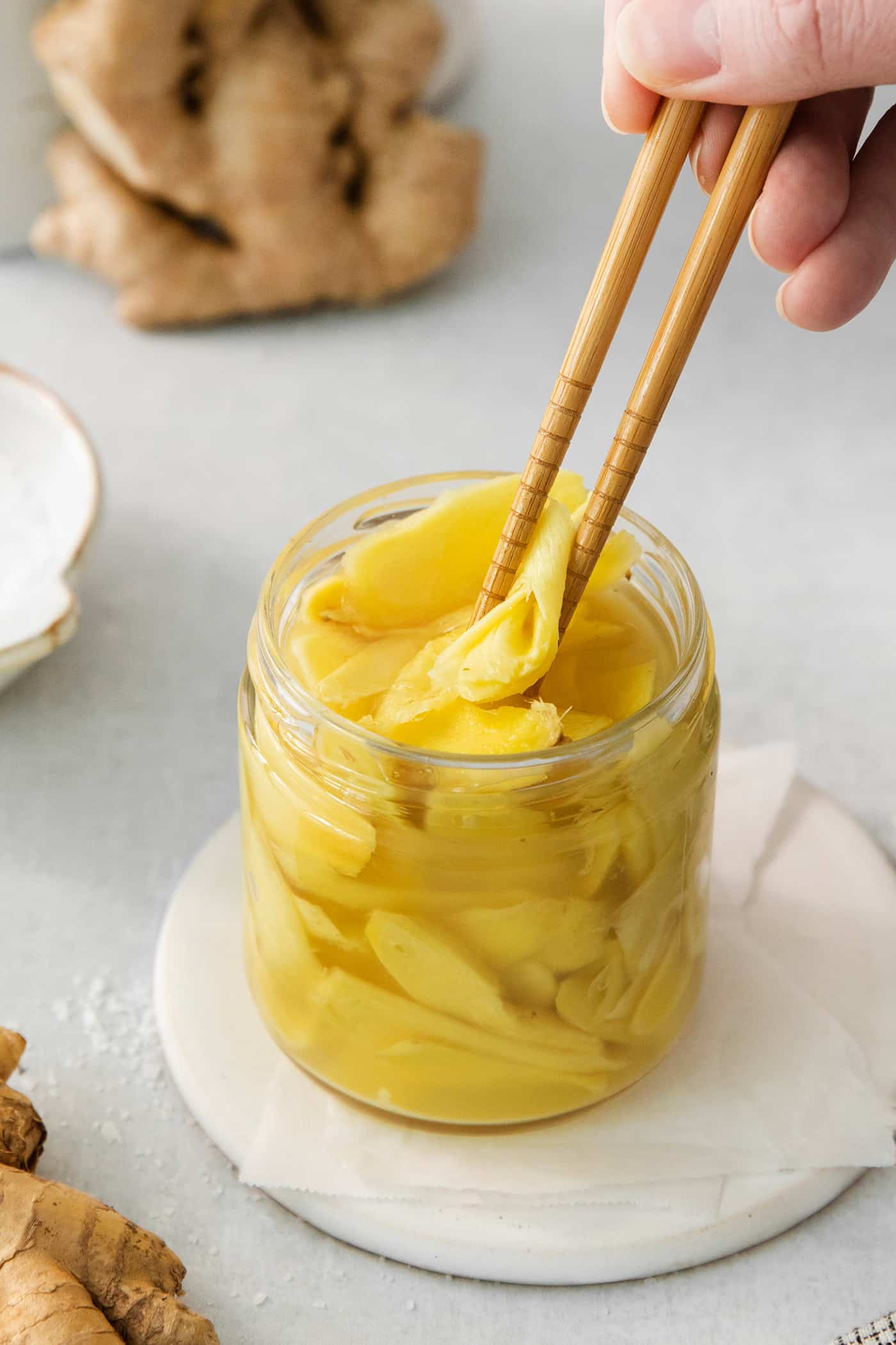Peppery, pink Pickled Ginger is a wonderful companion to sushi and it's so easy to make at home! You need just 5 ingredients. Chopsticks pick up a piece of pickled ginger.