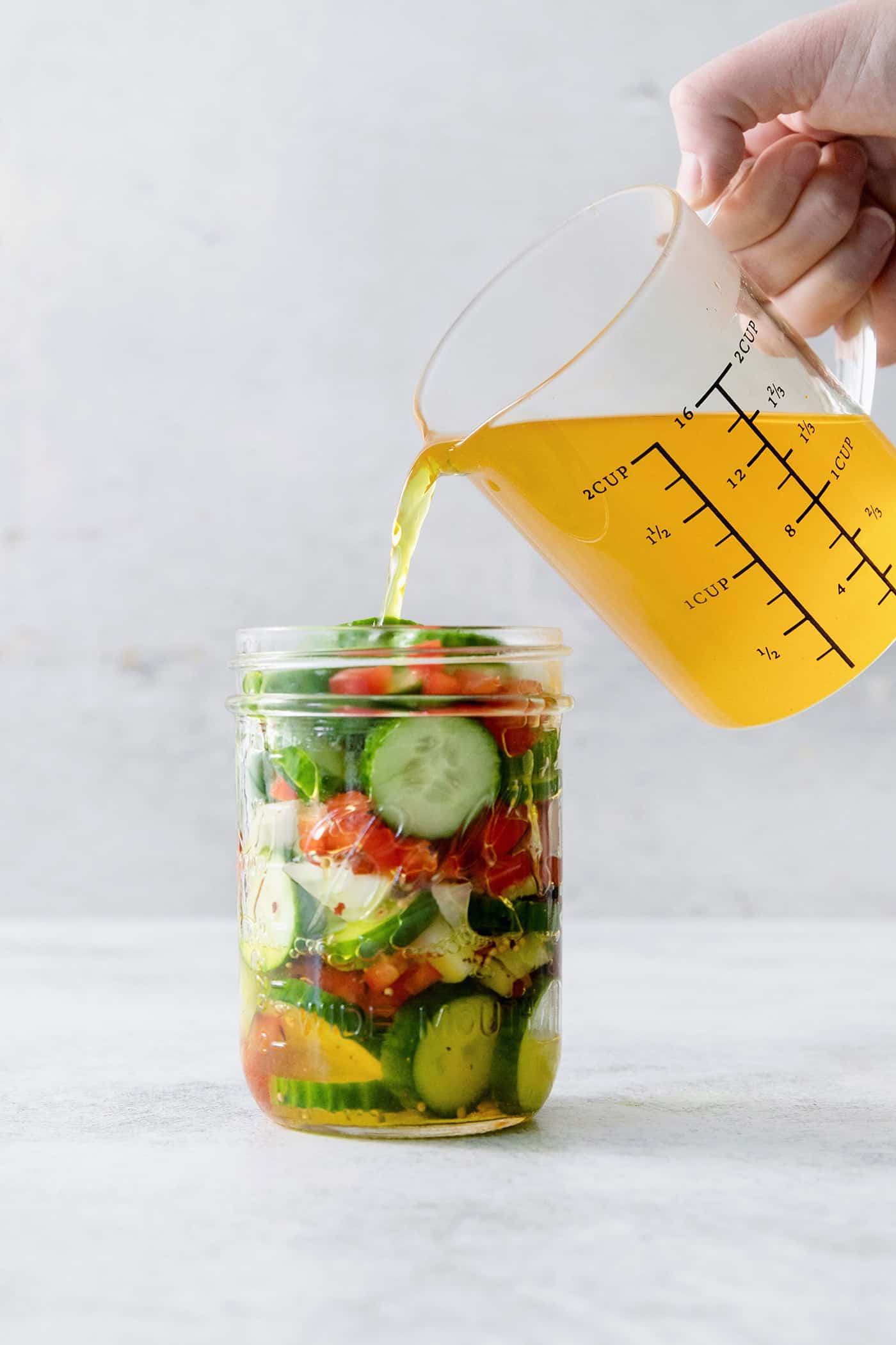 These homemade Sweet and Spicy Pickles are perfectly crisp with a bit of a bite. They're just right piled on burgers or as a snack. Brine is poured from a pitcher into a jar of vegetables to pickle them.