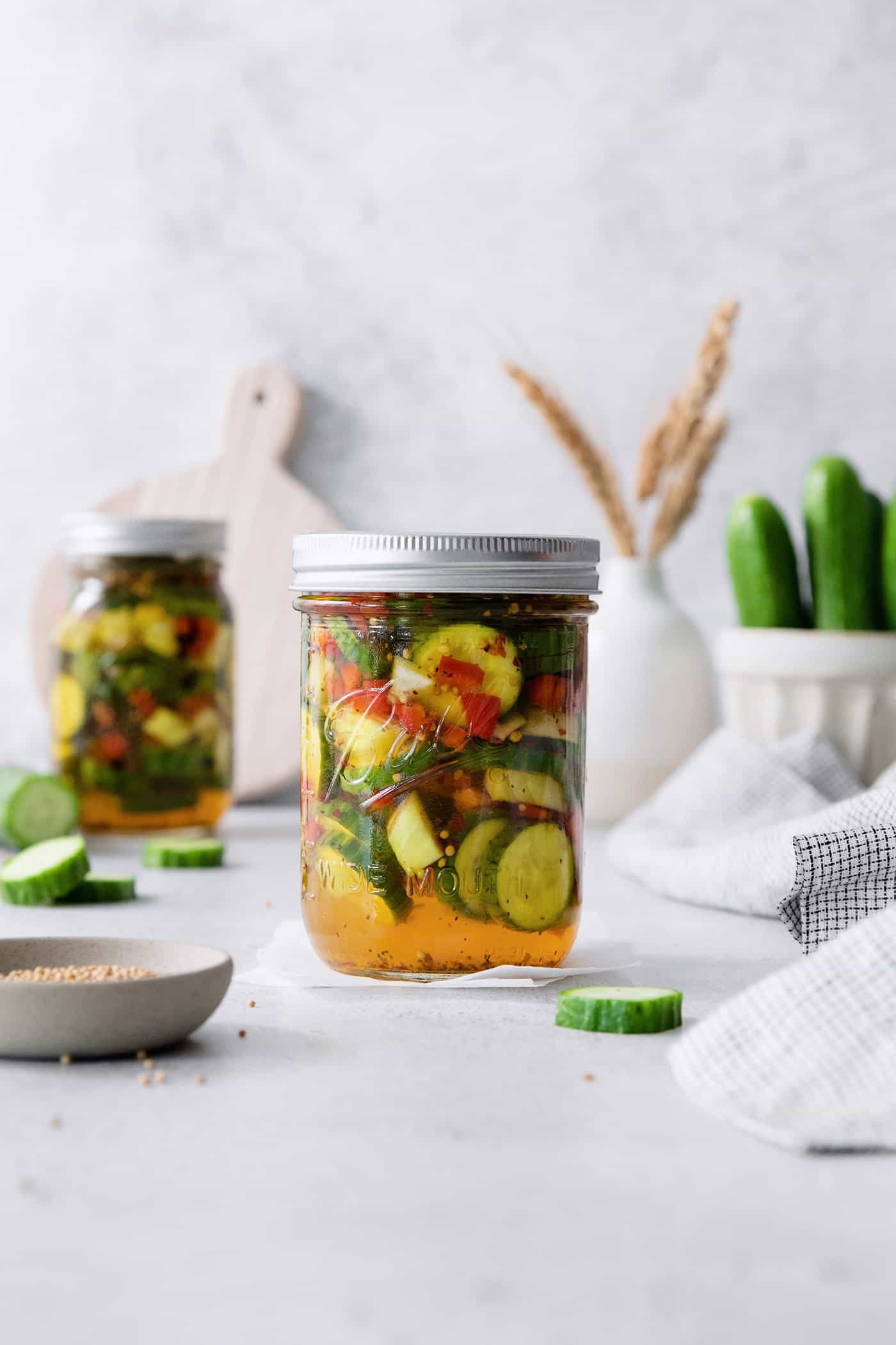 These homemade Sweet and Spicy Pickles are perfectly crisp with a bit of a bite. They're just right piled on burgers or as a snack. Jars of sweet and spicy pickles with cucumbers in the background.