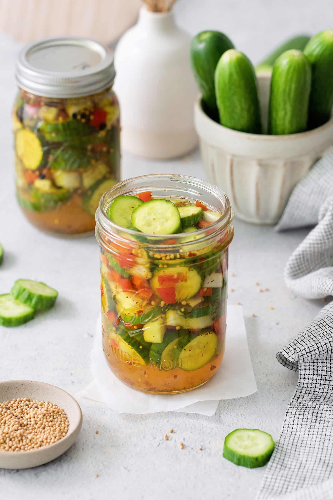These homemade Sweet and Spicy Pickles are perfectly crisp with a bit of a bite. They're just right piled on burgers or as a snack. Jars of sweet and spicy pickles with cucumbers in the background.