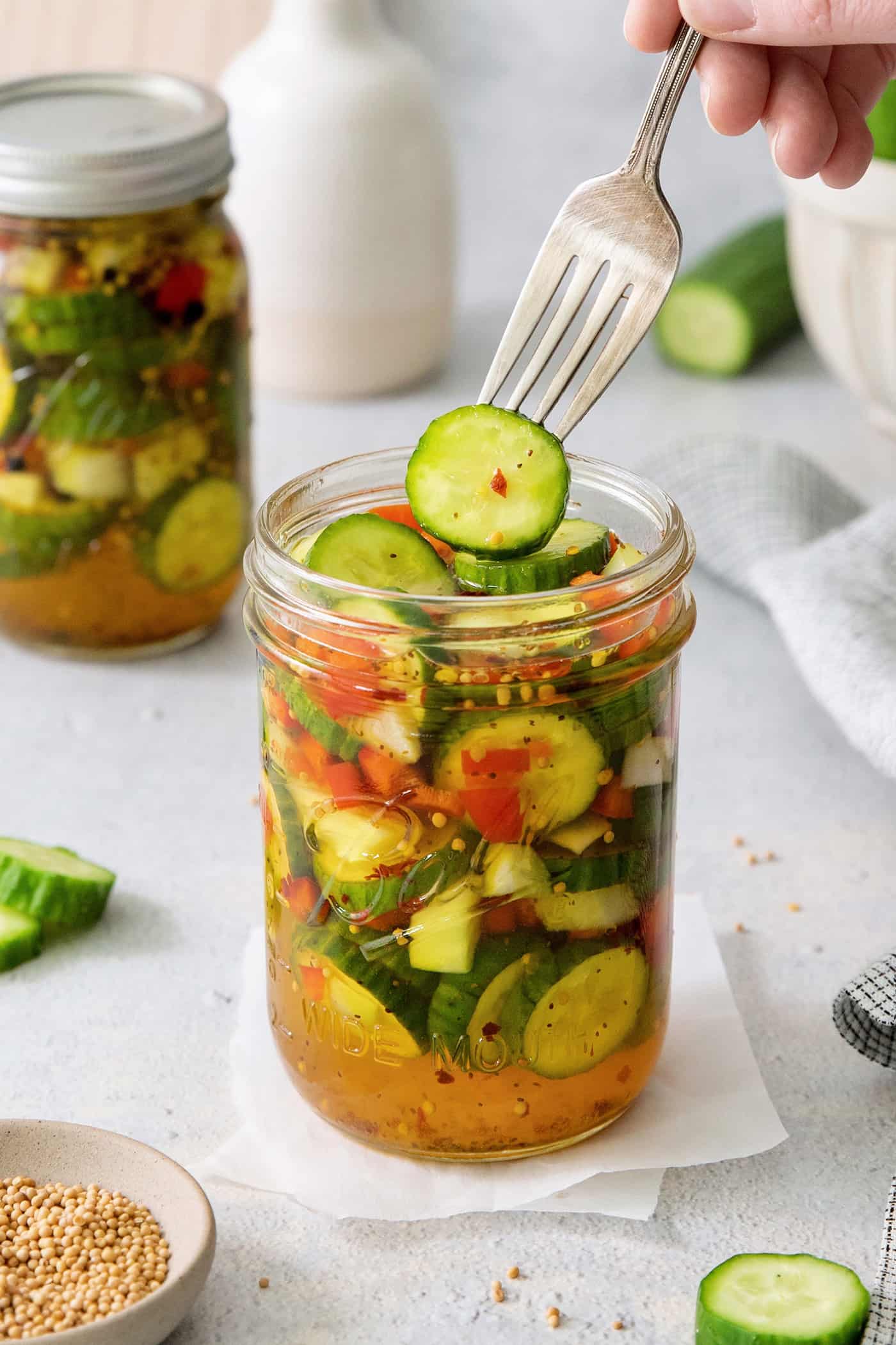 These homemade Sweet and Spicy Pickles are perfectly crisp with a bit of a bite. They're just right piled on burgers or as a snack. A fork holds a sweet and spicy pickle above a jar.