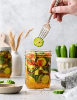 A fork holds a sweet and spicy pickle above a jar.