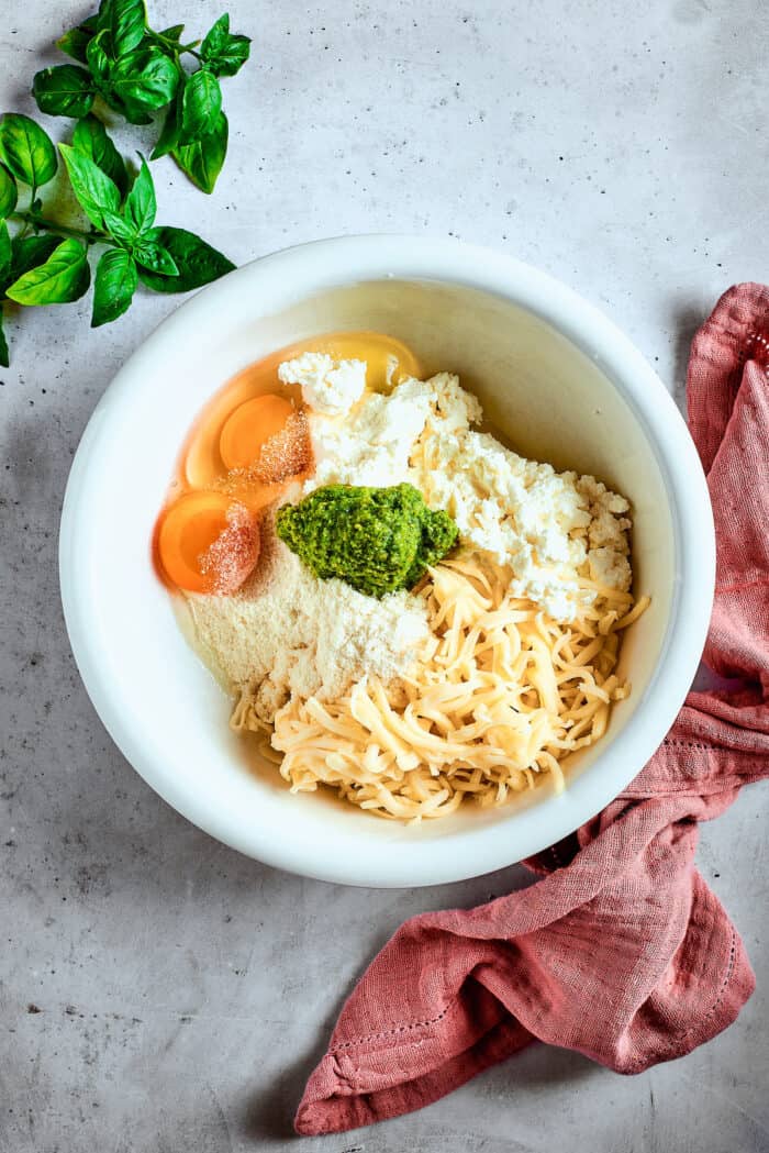 Cozy Stuffed Shells with Meat are packed with plenty of ground beef and a creamy, pesto-spiked filling to make a hearty meal. Eggs are mixed into filling for stuffed shells in a white bowl.