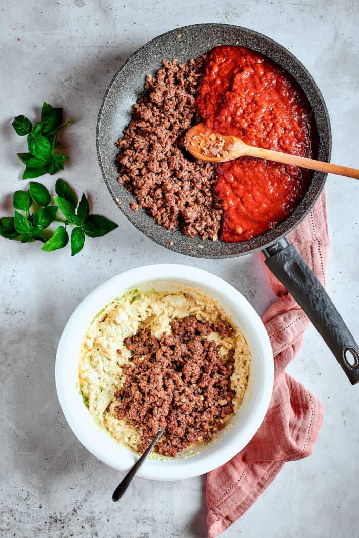 Cozy Stuffed Shells with Meat are packed with plenty of ground beef and a creamy, pesto-spiked filling to make a hearty meal. Ground beef is combined with tomato sauce in a skillet with a wooden spoon.
