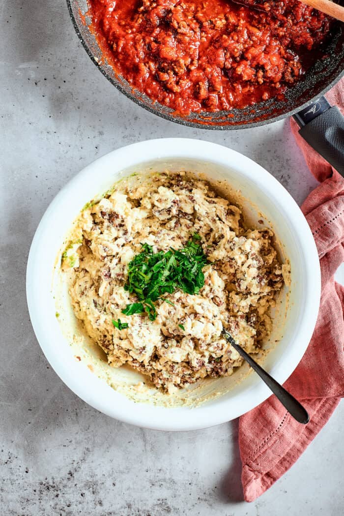 Cozy Stuffed Shells with Meat are packed with plenty of ground beef and a creamy, pesto-spiked filling to make a hearty meal. Filling for stuffed shells is shown in a bowl.