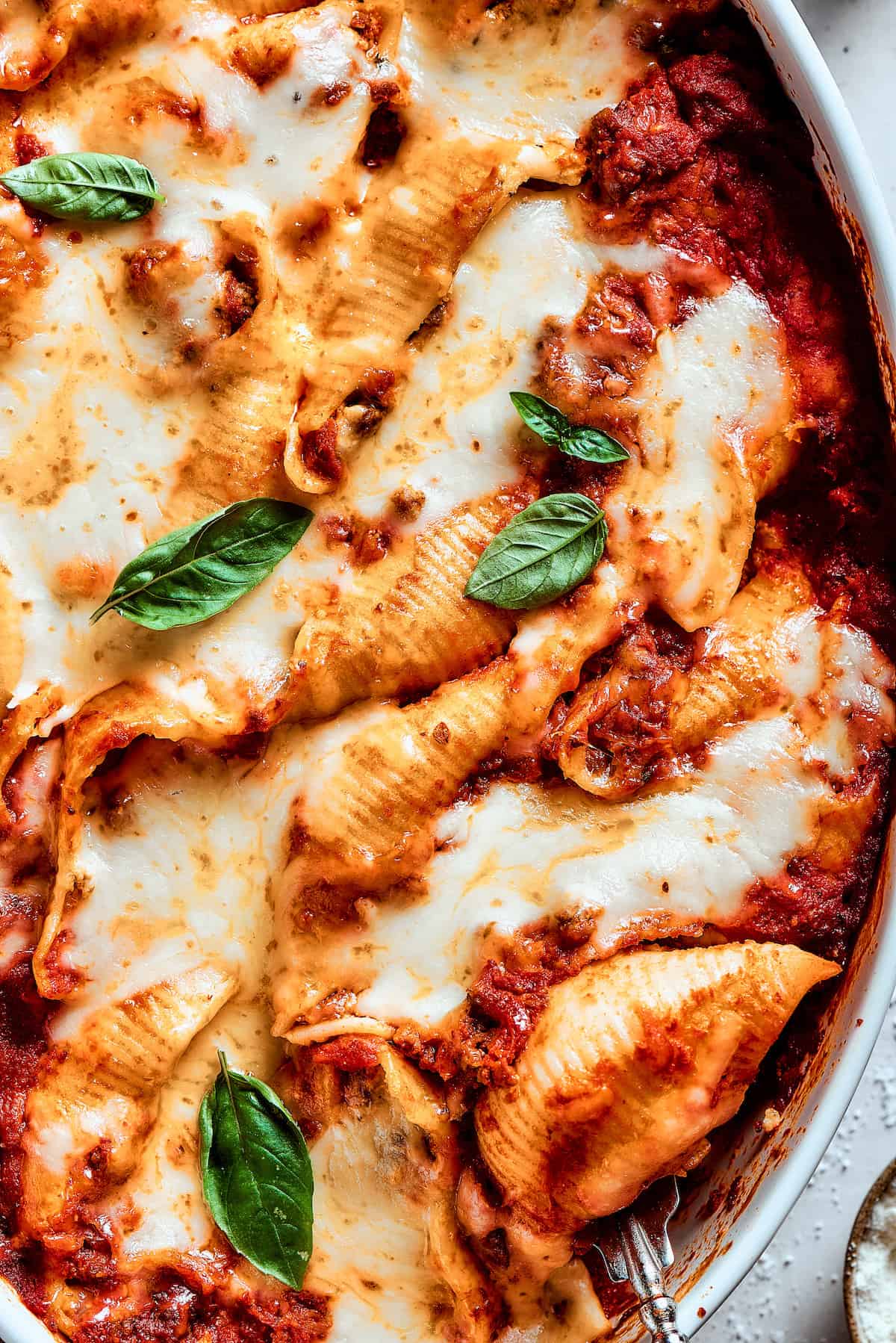 Cozy Stuffed Shells with Meat are packed with plenty of ground beef and a creamy, pesto-spiked filling to make a hearty meal. Close up shot of a pan of stuffed shells.