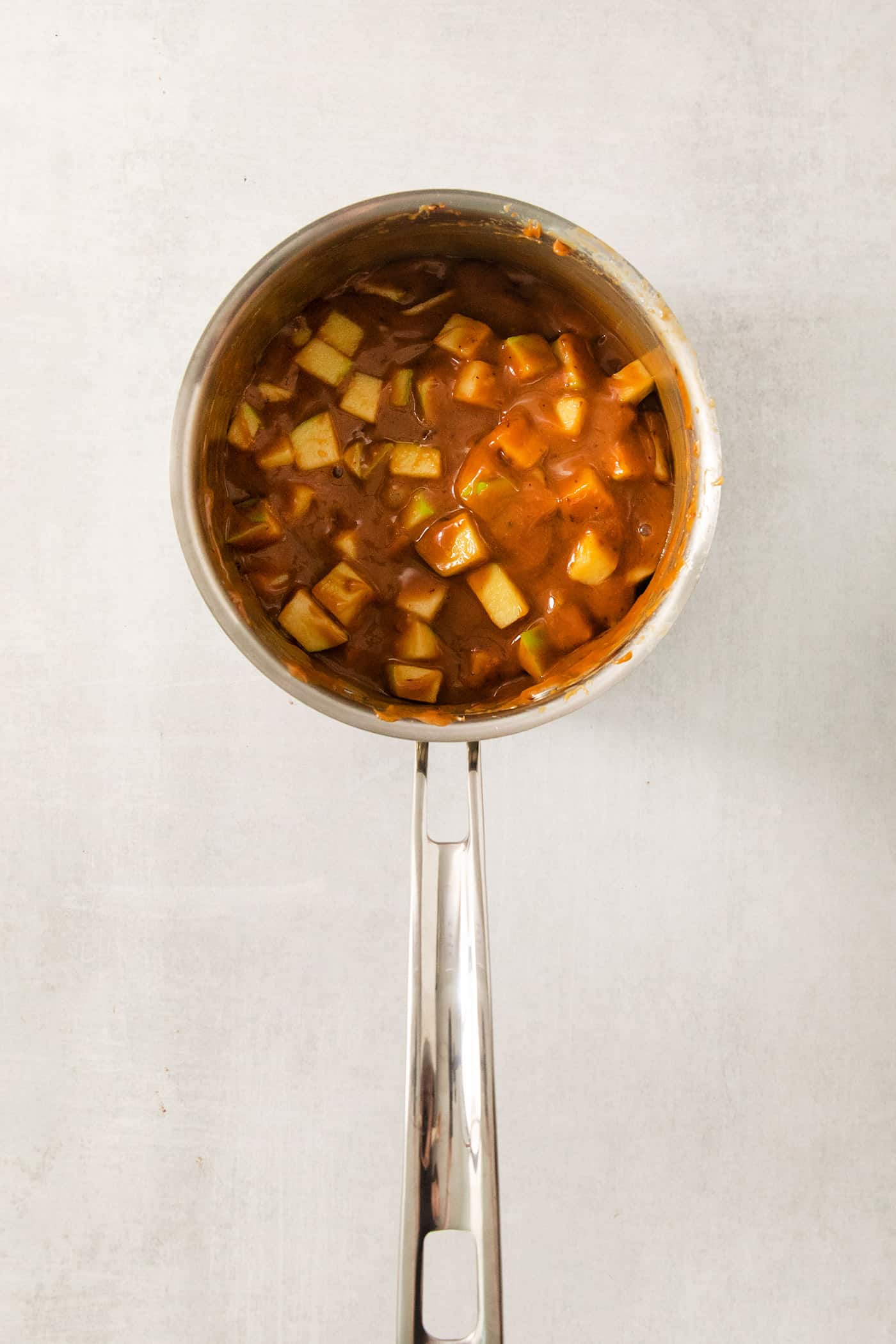 This Caramel Apple Bark is a fun treat to make when you want the flavor of a fresh caramel apple without the hassle. An overhead shot of a pot of caramel and chopped apples.