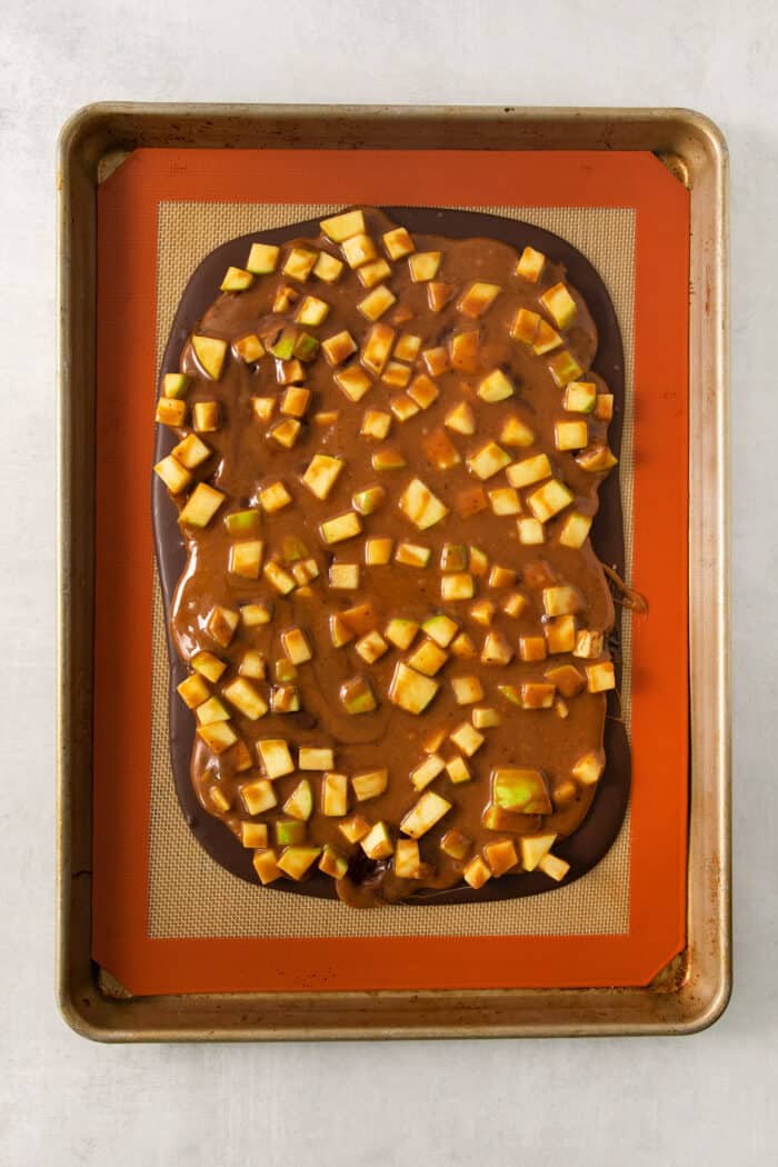 This Caramel Apple Bark is a fun treat to make when you want the flavor of a fresh caramel apple without the hassle. A layer of chocolate is topped with a layer of caramel and apples on a baking sheet.