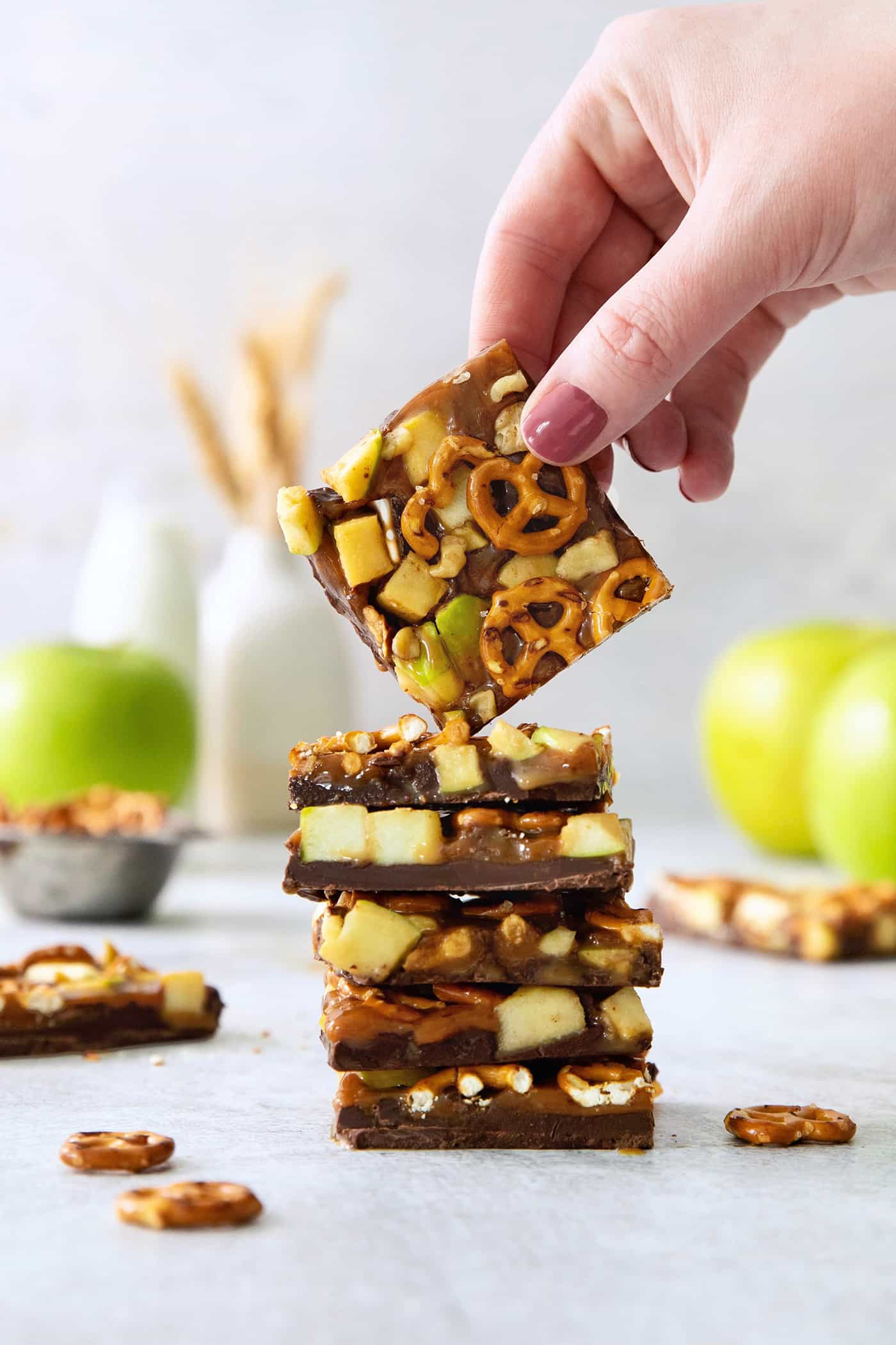 This Caramel Apple Bark is a fun treat to make when you want the flavor of a fresh caramel apple without the hassle. A hand lifts up a piece of caramel apple bark from a stack of bark.