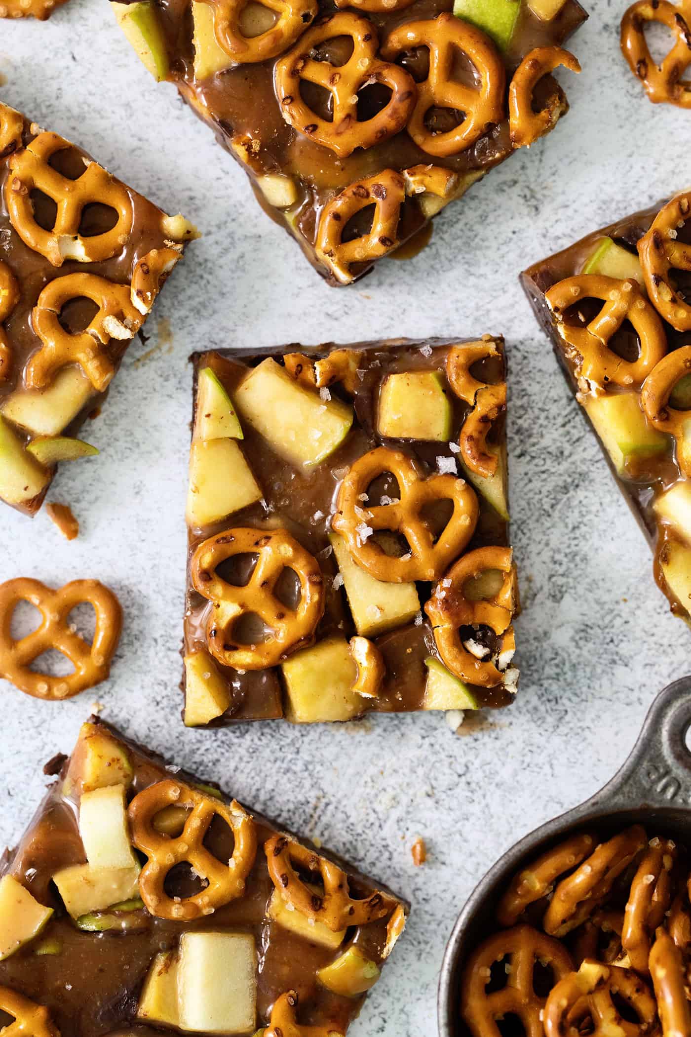 This Caramel Apple Bark is a fun treat to make when you want the flavor of a fresh caramel apple without the hassle. An overhead shot of pieces of caramel apple bark with pretzels on a white background.