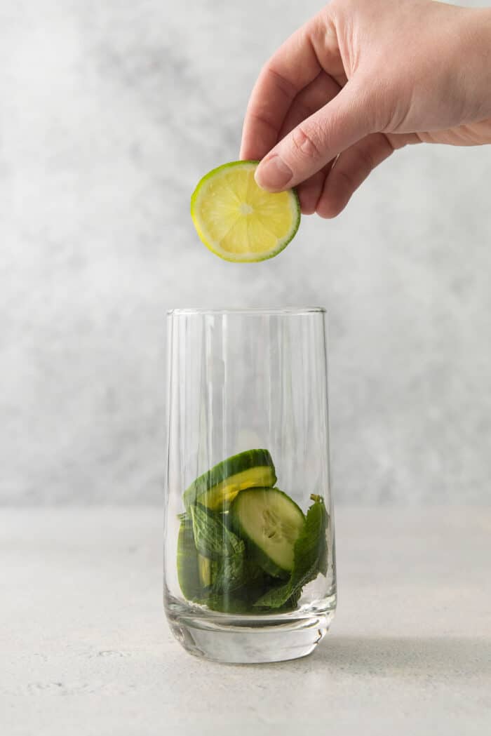 A Cucumber Mojito takes your classic mojito recipe and adds orange liqueur and cucumber slices for a refreshing twist on a minty favorite. A hand adds limes to a glass for a cucumber mojito.