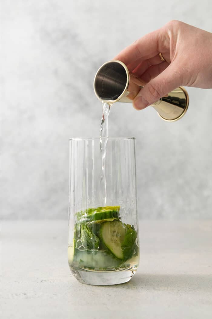 A Cucumber Mojito takes your classic mojito recipe and adds orange liqueur and cucumber slices for a refreshing twist on a minty favorite. A hand pours in orange liqueur for a cucumber mojito.