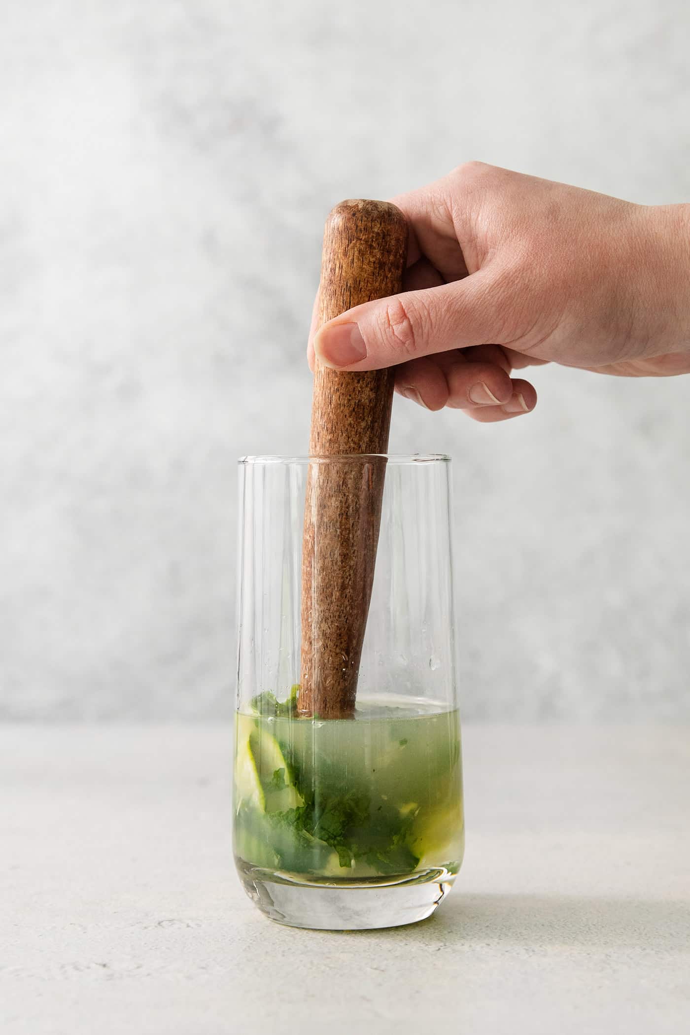A Cucumber Mojito takes your classic mojito recipe and adds orange liqueur and cucumber slices for a refreshing twist on a minty favorite. A hand uses a wooden pestle to muddle ingredients for a cucumber mojito.