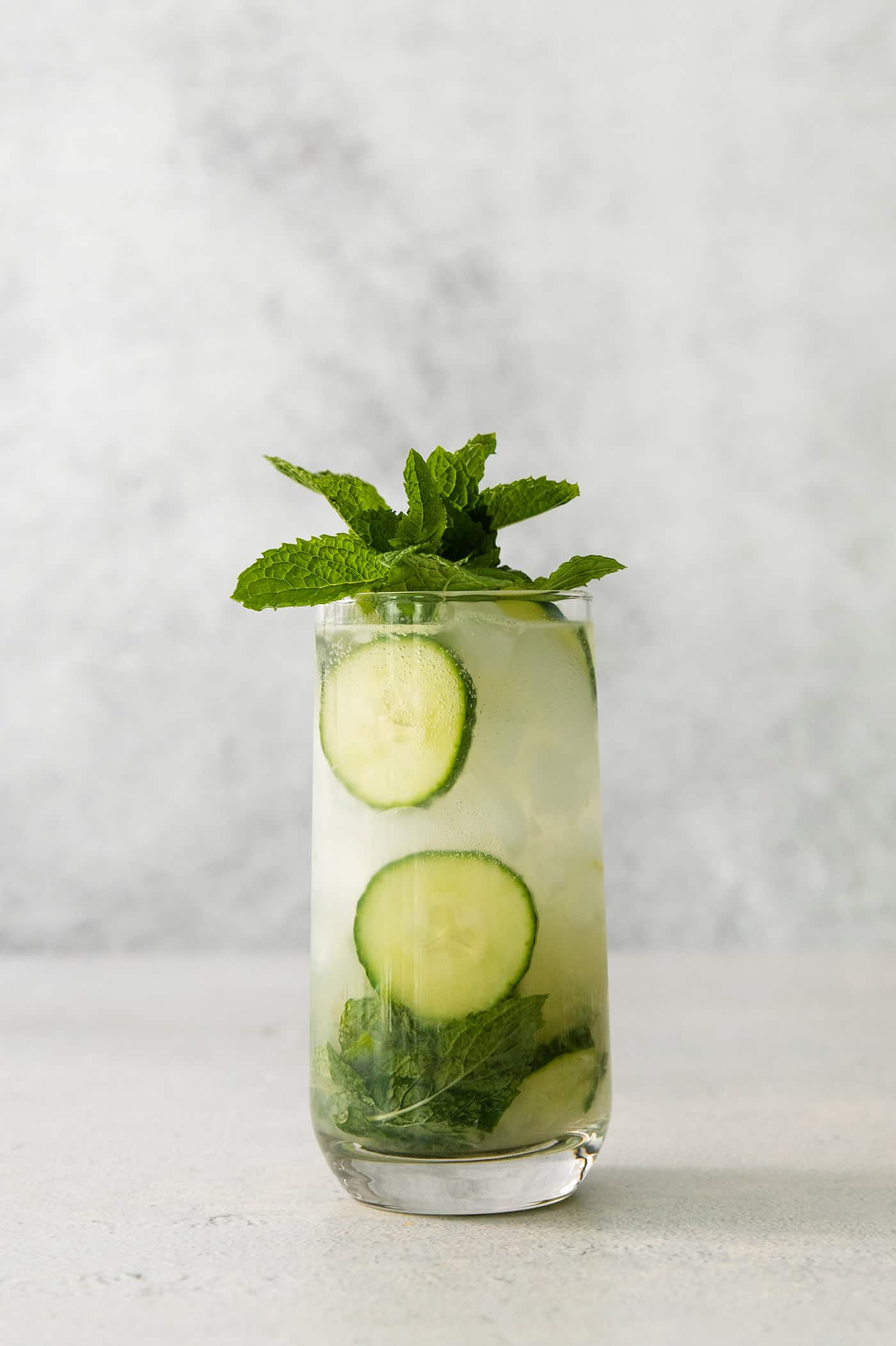 A Cucumber Mojito takes your classic mojito recipe and adds orange liqueur and cucumber slices for a refreshing twist on a minty favorite. A glass of cucumber mojito topped with basil leaves.