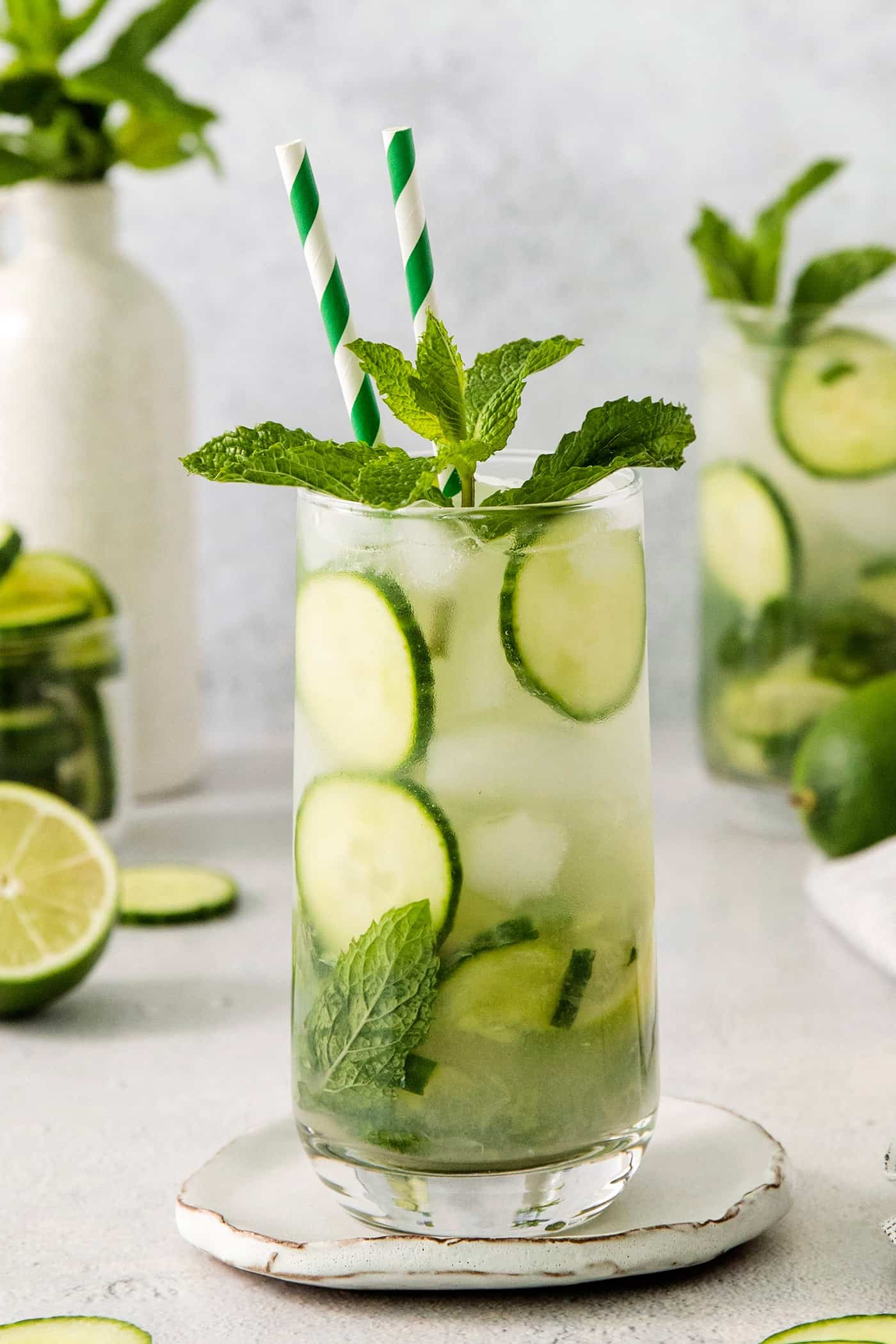 A Cucumber Mojito takes your classic mojito recipe and adds orange liqueur and cucumber slices for a refreshing twist on a minty favorite. A tall glass of cucumber mojito garnished with cucumber and mint and finished with two green straws.
