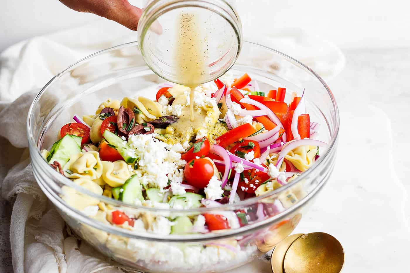 Dressing is poured onto a bowl of tortellini salad.