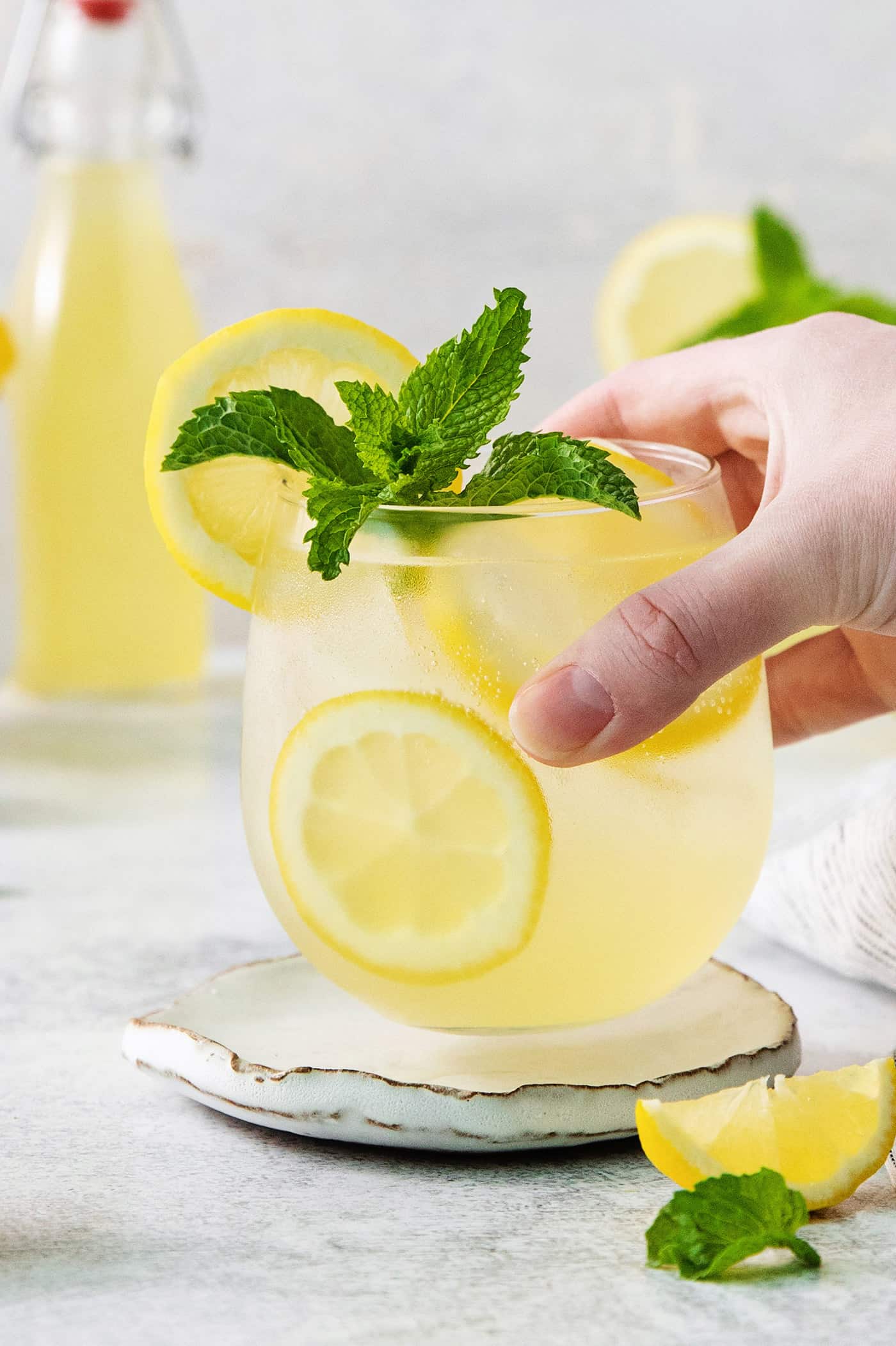 This Limoncello Spritz is fruity and refreshing, lightly sweet, and has a fun effervescence. It’s the perfect summer drink! A hand holds a glass of limoncello spritz garnished with mint.