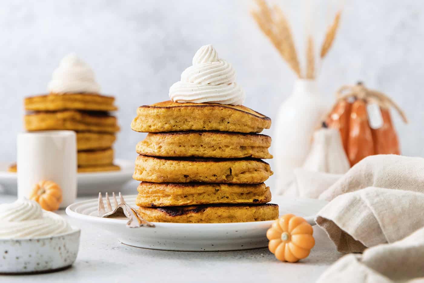 These Pumpkin Pancakes are rich and fluffy, flavored with buttermilk, pumpkin puree, and pumpkin pie spice for the perfect fall breakfast! A stack of pumpkin pancakes topped with maple cinnamon whipped cream on a white plate.