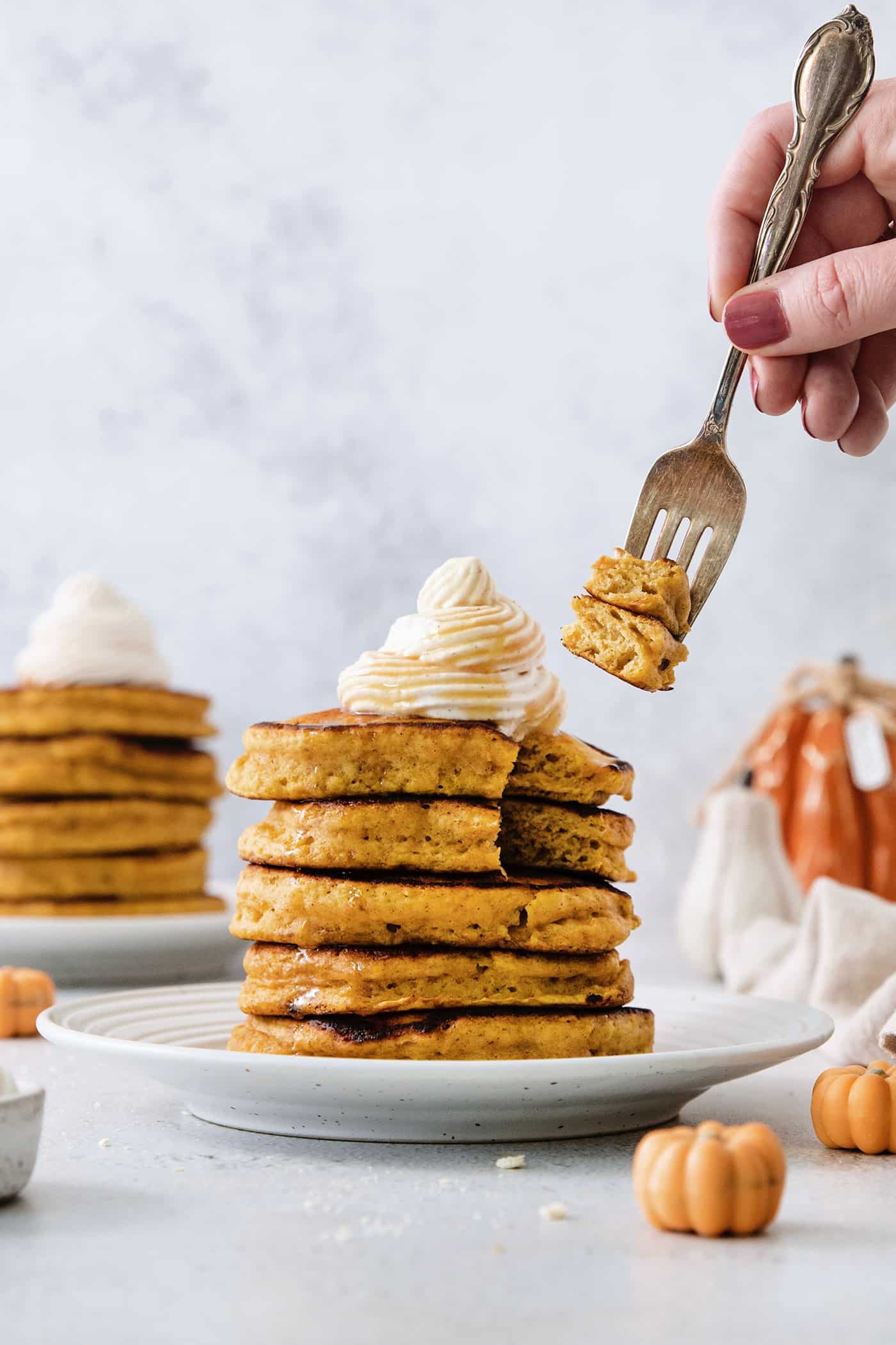 These Pumpkin Pancakes are rich and fluffy, flavored with buttermilk, pumpkin puree, and pumpkin pie spice for the perfect fall breakfast! A fork holds pieces of pumpkin pancakes cut out of a stack of pancakes with more pancakes in the background.