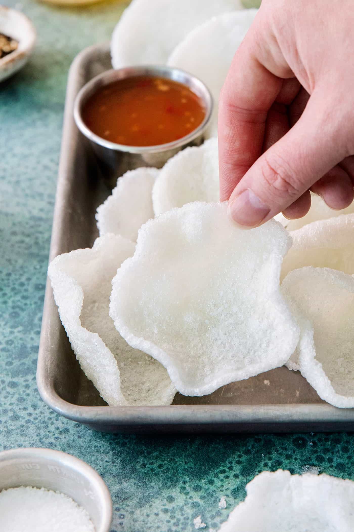Shrimp Chips are a quick snack that will satisfy your craving for something with a salty crunch and a light umami flavor. A hand lifts a shrimp chip.