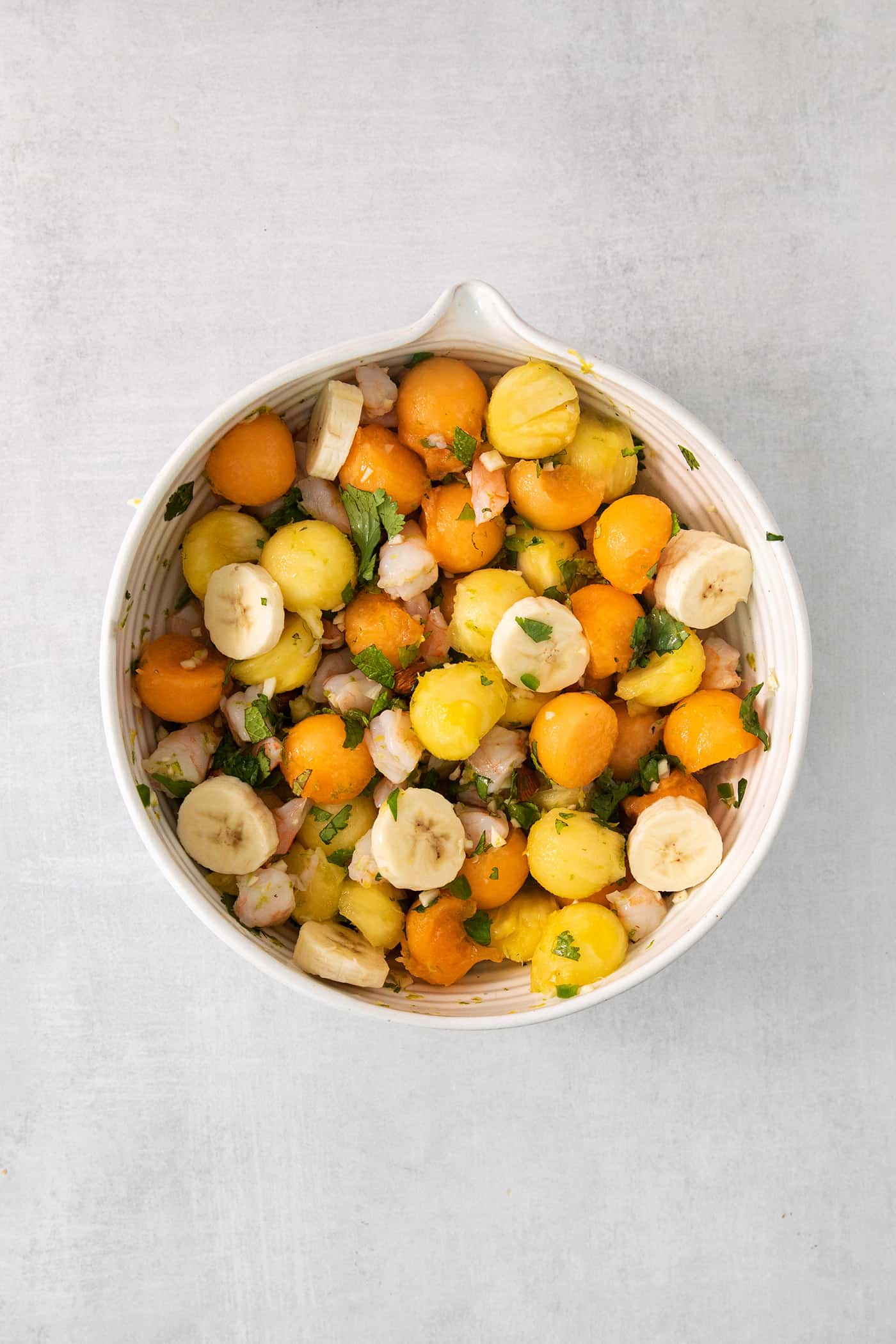 This Tropical Shrimp Salad has fresh, bright color and flavor. It's a unique, refreshing appetizer or salad recipe, great for entertaining! Melon, banana, and pineapple is added to a white bowl of tropical shrimp salad, shown on a white background.