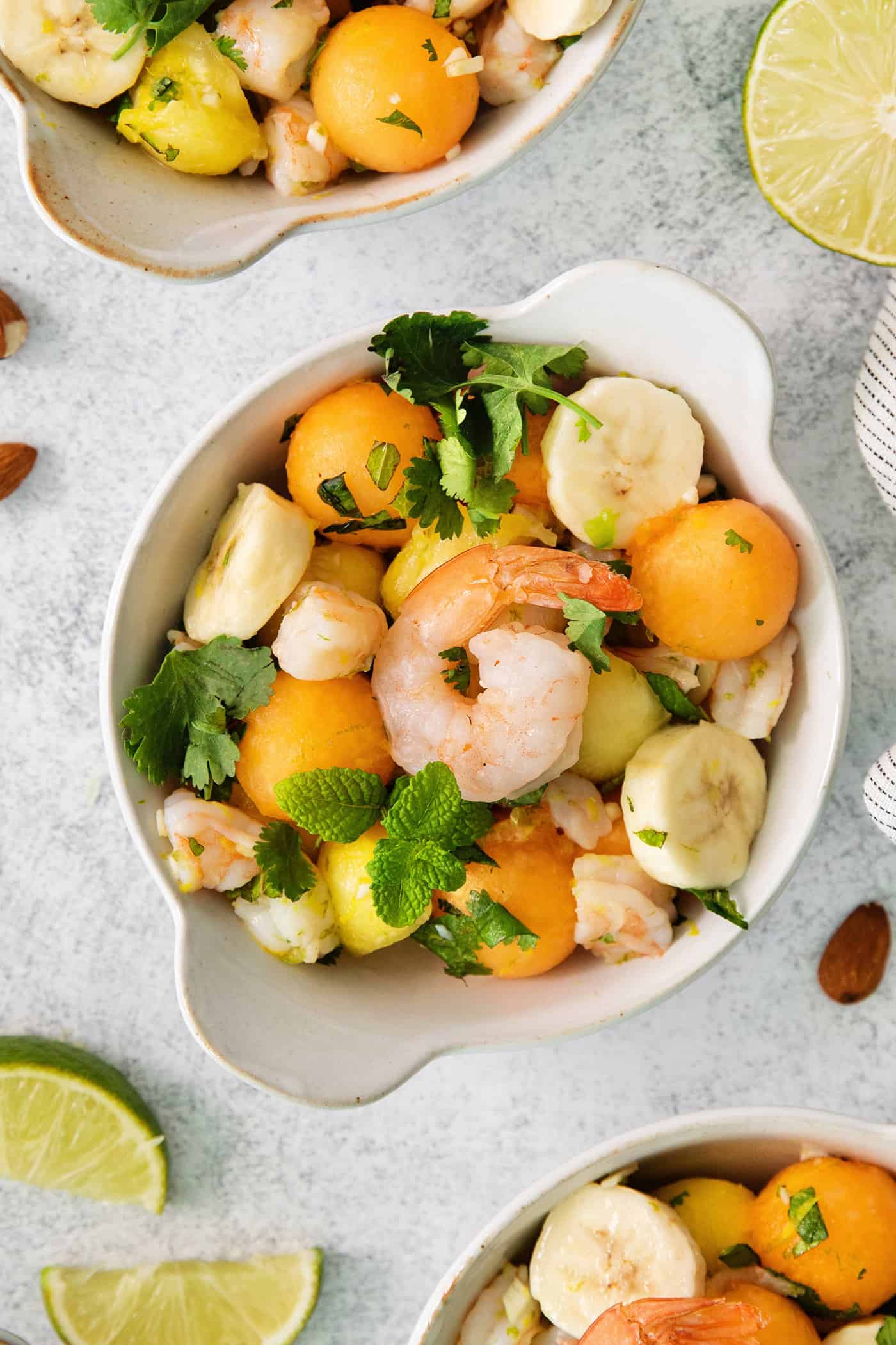 This Tropical Shrimp Salad has fresh, bright color and flavor. It's a unique, refreshing appetizer or salad recipe, great for entertaining! An overhead shot of a colorful bowl of tropical shrimp salad with fruit, shrimp, and mint leaves.