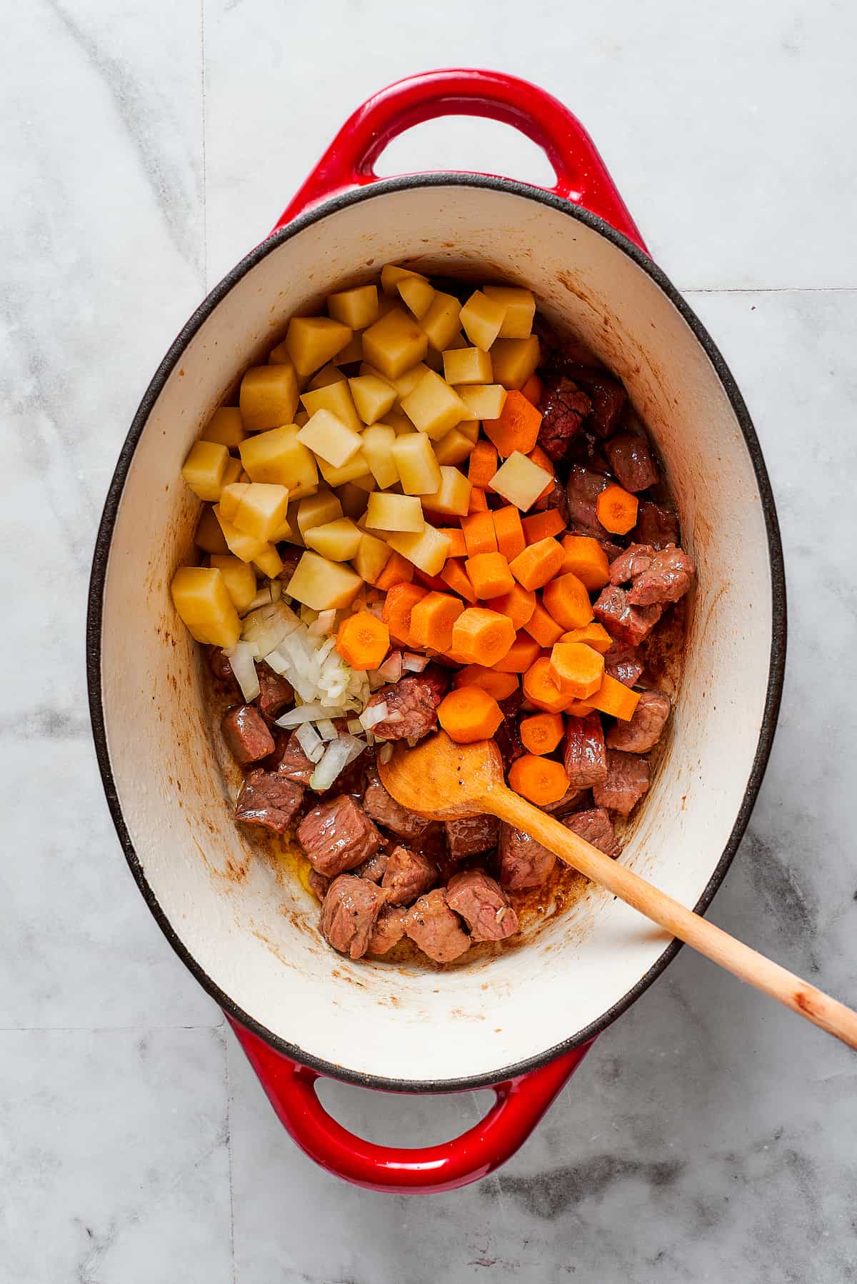 Comforting Beef Pot Pie is packed with tender beef and vegetables tucked into a stout-based gravy with flaky pie crust balanced on top. Meat and vegetables are shown added to a Dutch oven for beef pot pie.