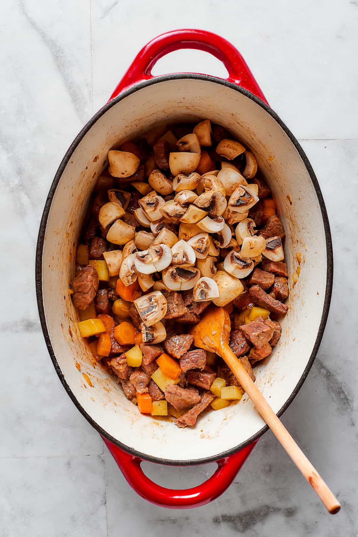 Comforting Beef Pot Pie is packed with tender beef and vegetables tucked into a stout-based gravy with flaky pie crust balanced on top. A wooden spoon stirs together ingredients in a Dutch oven for beef pot pie.