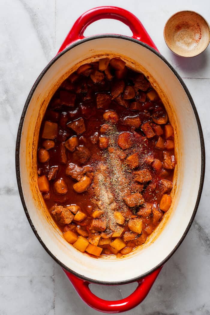 Comforting Beef Pot Pie is packed with tender beef and vegetables tucked into a stout-based gravy with flaky pie crust balanced on top. Spices are stirred into a pot of beef pot pie filling.