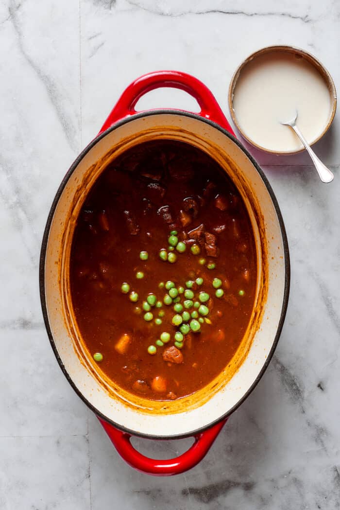 Comforting Beef Pot Pie is packed with tender beef and vegetables tucked into a stout-based gravy with flaky pie crust balanced on top. Peas are added to a pot of pot pie filling.