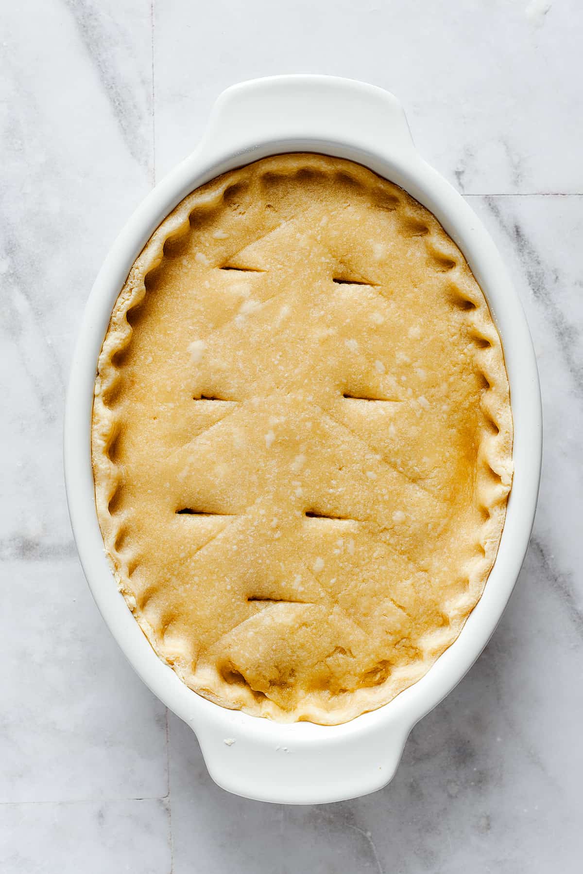 Comforting Beef Pot Pie is packed with tender beef and vegetables tucked into a stout-based gravy with flaky pie crust balanced on top. A white oval pie dish is topped with crust for pot pie filling.